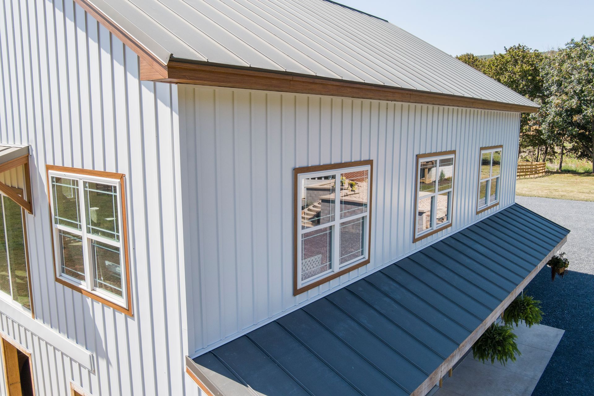 A white board-and-batten building with a dark metal roof, copper-colored trim, and several white-framed windows.