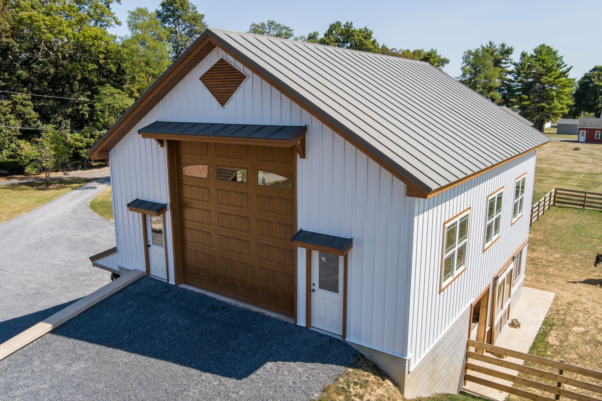 A white metal pole barn with brown trim, a large garage door, and two entry doors, with a metal roof.