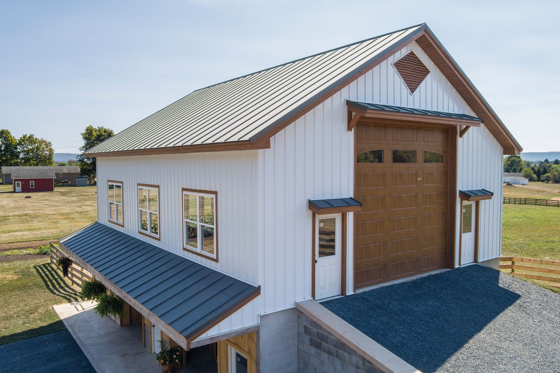 A white, board-and-batten pole barn with a dark metal roof, large wooden garage door, and side windows in a rural setting.