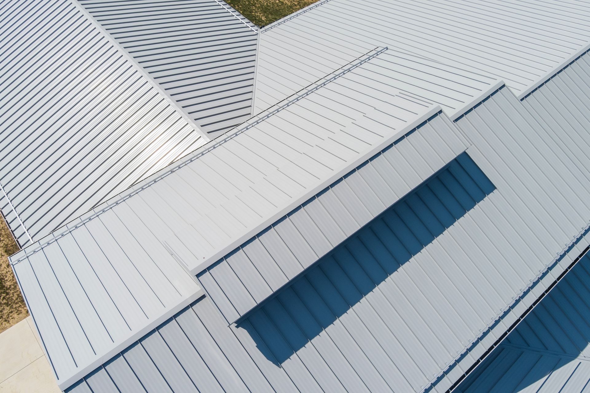 High-angle aerial view of a gray, multi-pitched metal roof with a rectangular skylight.