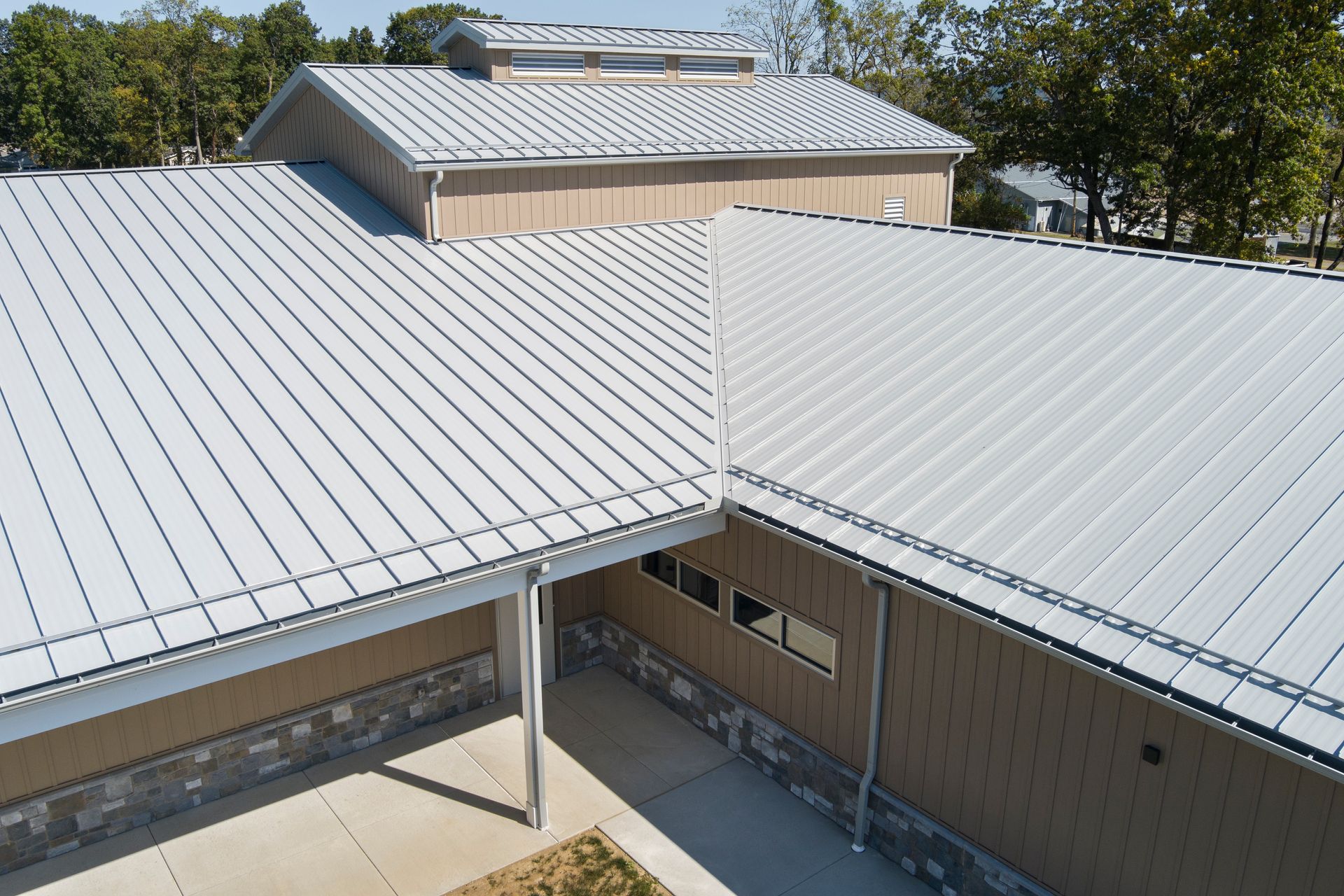 An aerial view of a building with a light gray metal roof, featuring a small courtyard and stone siding.
