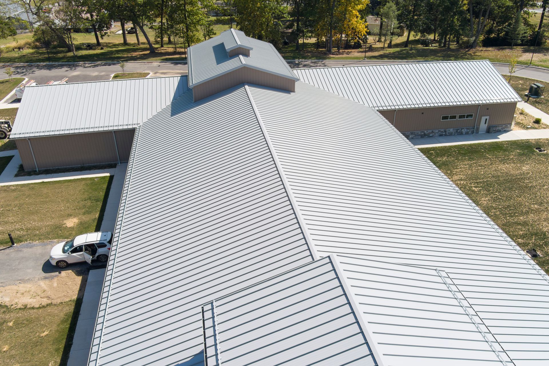 Aerial view of a building metal roof with a distinctive gray and white circular geometric pattern, surrounded by green lawns.