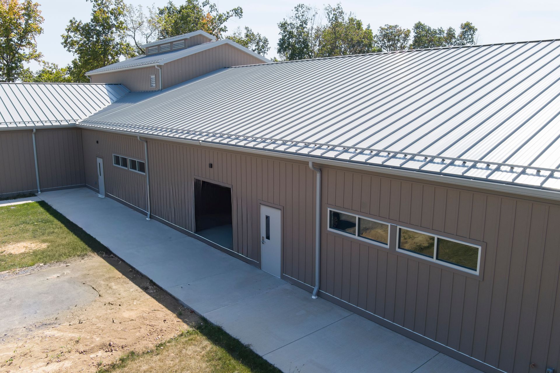 An elevated view of a brown, metal-sided building with a silver standing-seam roof, windows, and a paved walkway.
