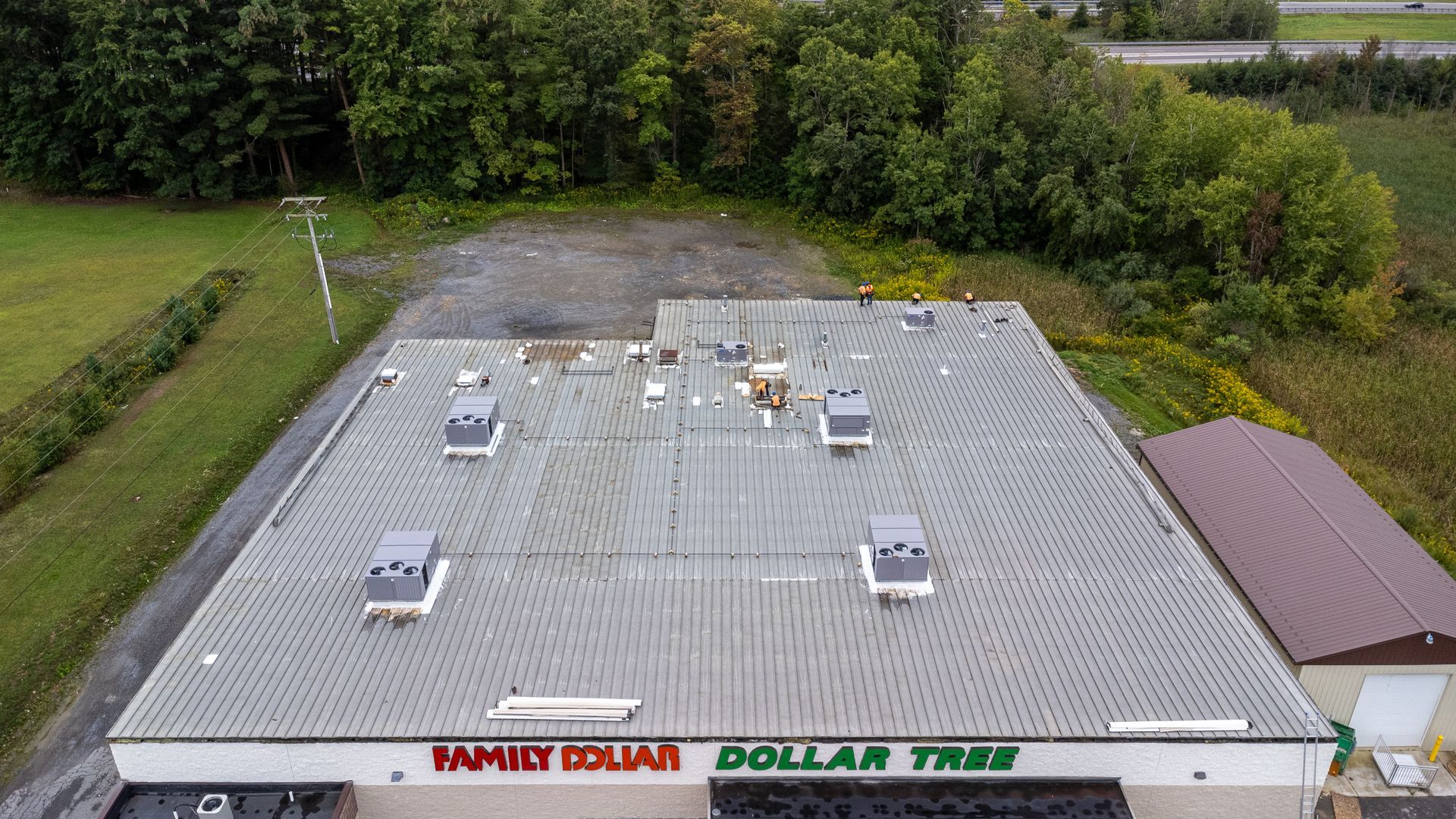 Aerial view of a Family Dollar and Dollar Tree store with a corrugated metal roof and surrounding trees.
