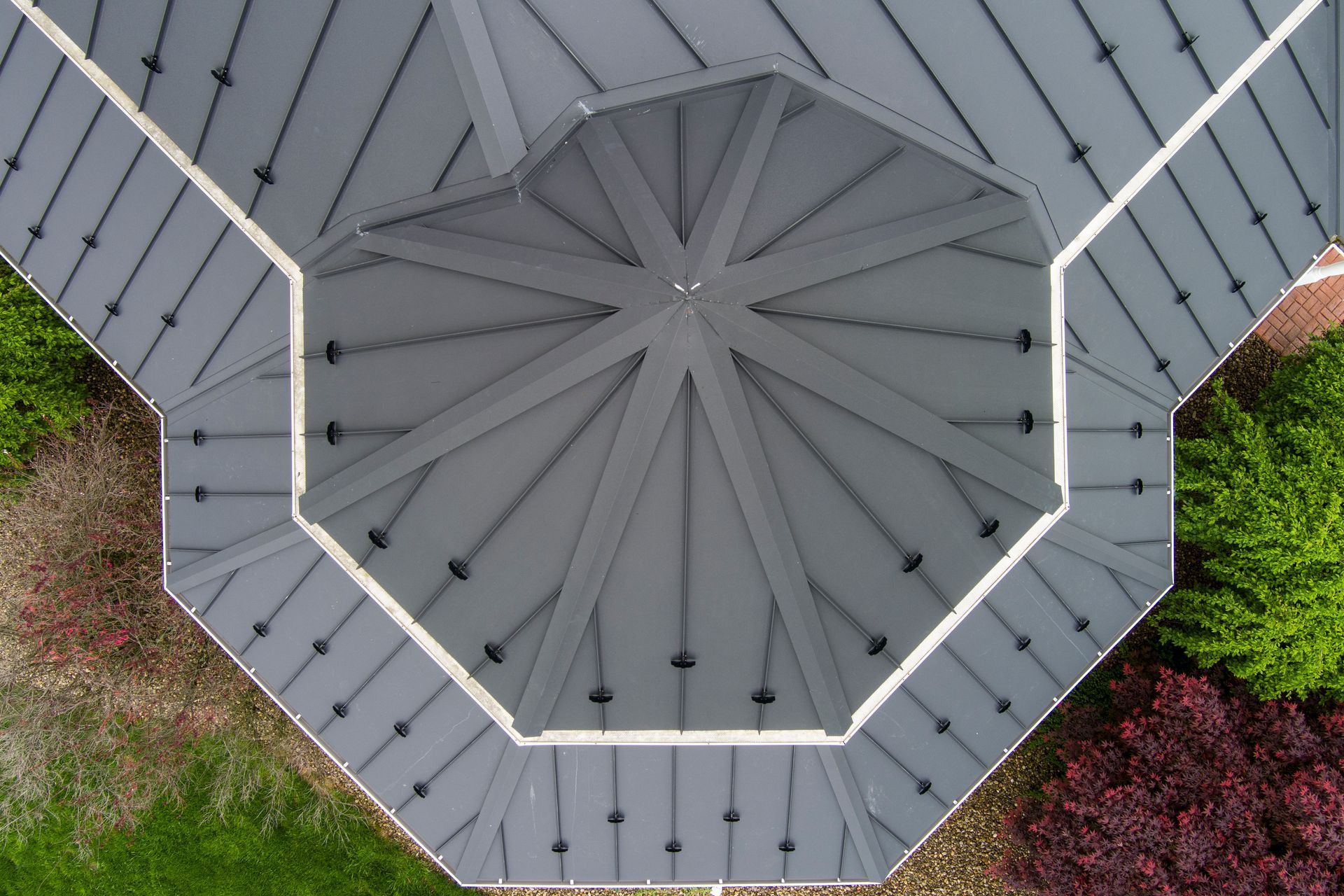 Overhead view of a grey octagonal gazebo roof with a central decorative structure, surrounded by greenery.