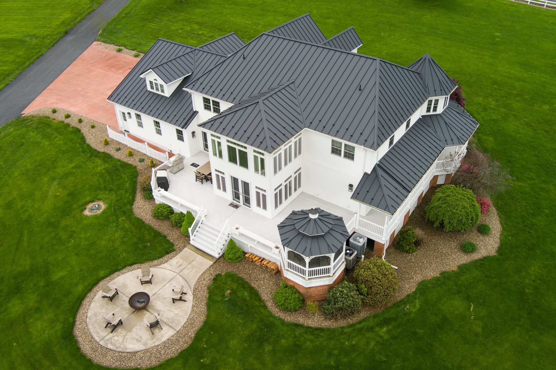 Aerial view of a white, multi-level house with a dark gray roof, surrounded by green grass and a brick patio.