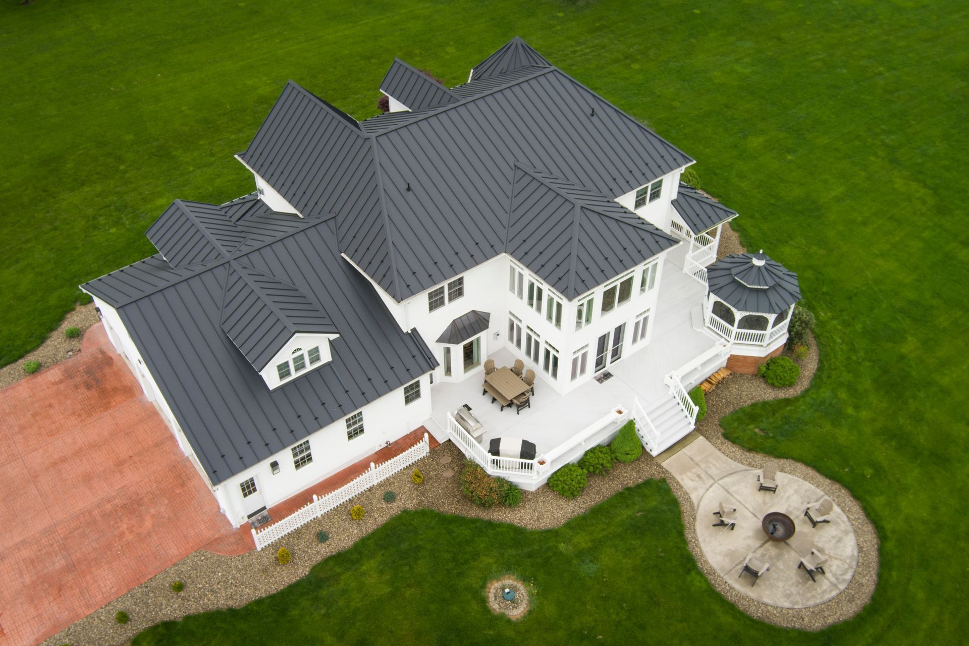 White house with a dark gray roof, a large deck, and a gazebo, on a green lawn.