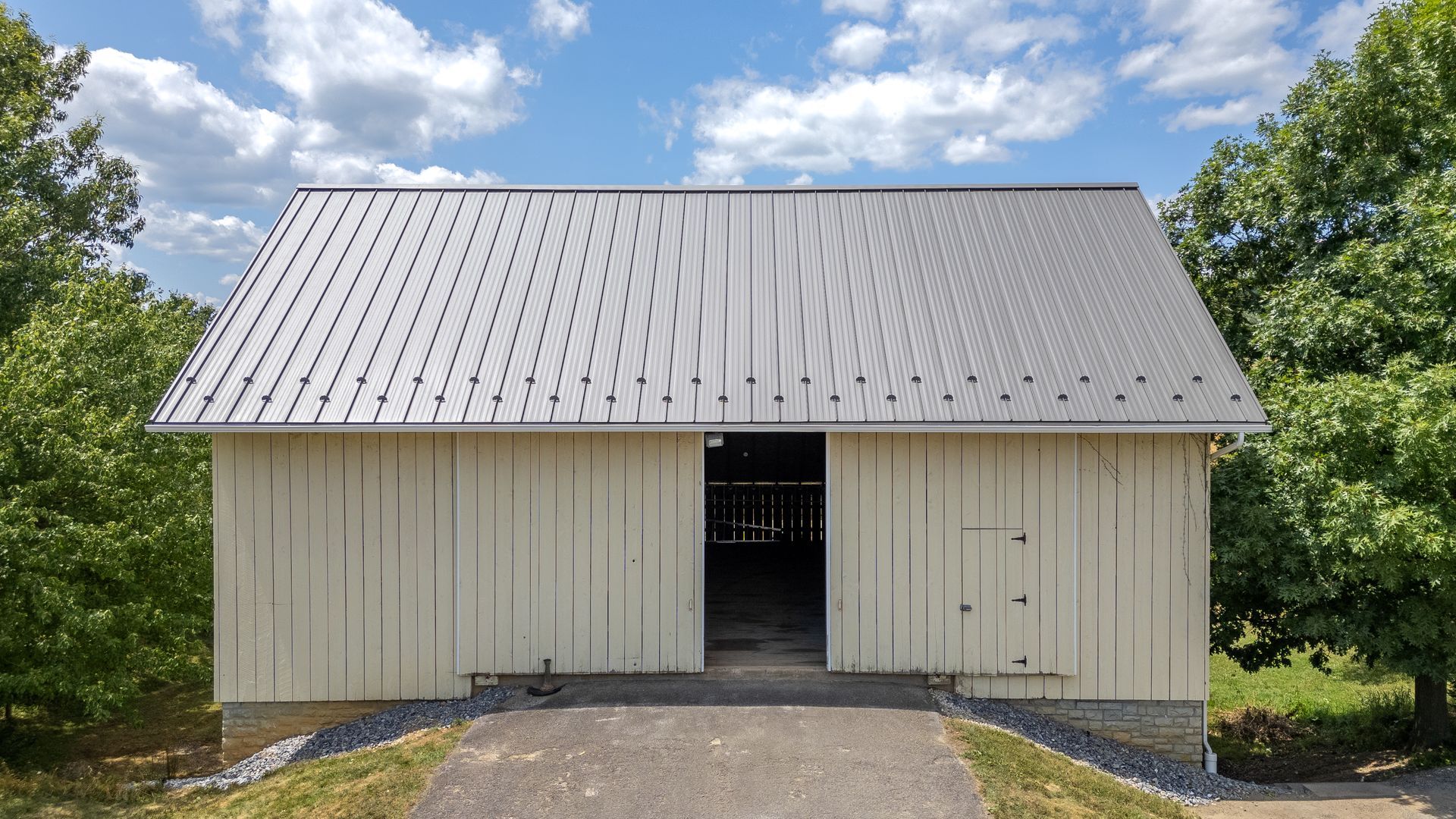White barn with open doors, gravel path, metal roof, sunny day.