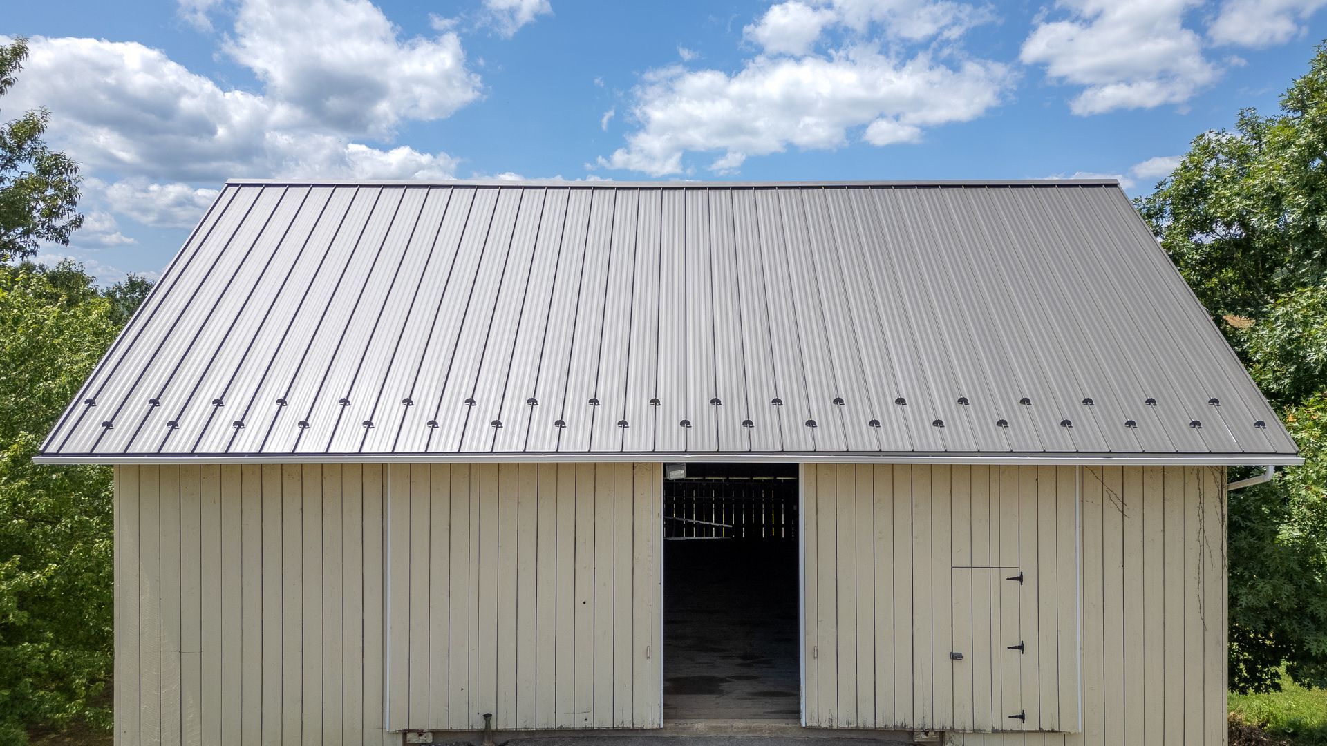 White barn with a silver metal roof, open doorway, and blue sky background.