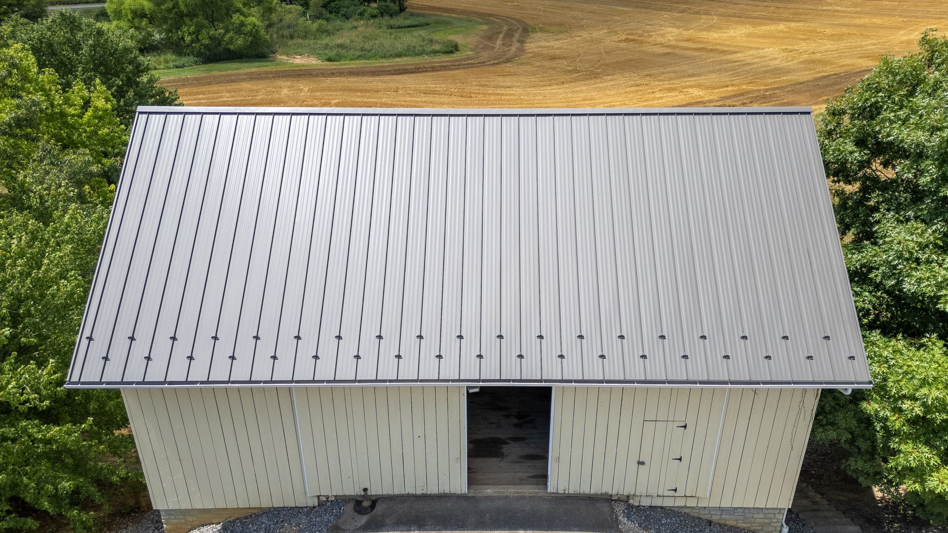 White barn with a silver metal roof and trees in the background.