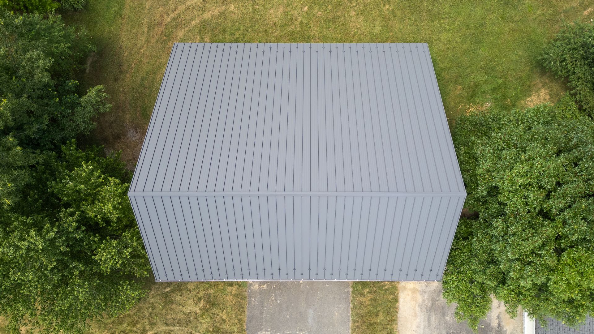Overhead view of gray rectangular building with patterned roof, surrounded by green foliage and grass.