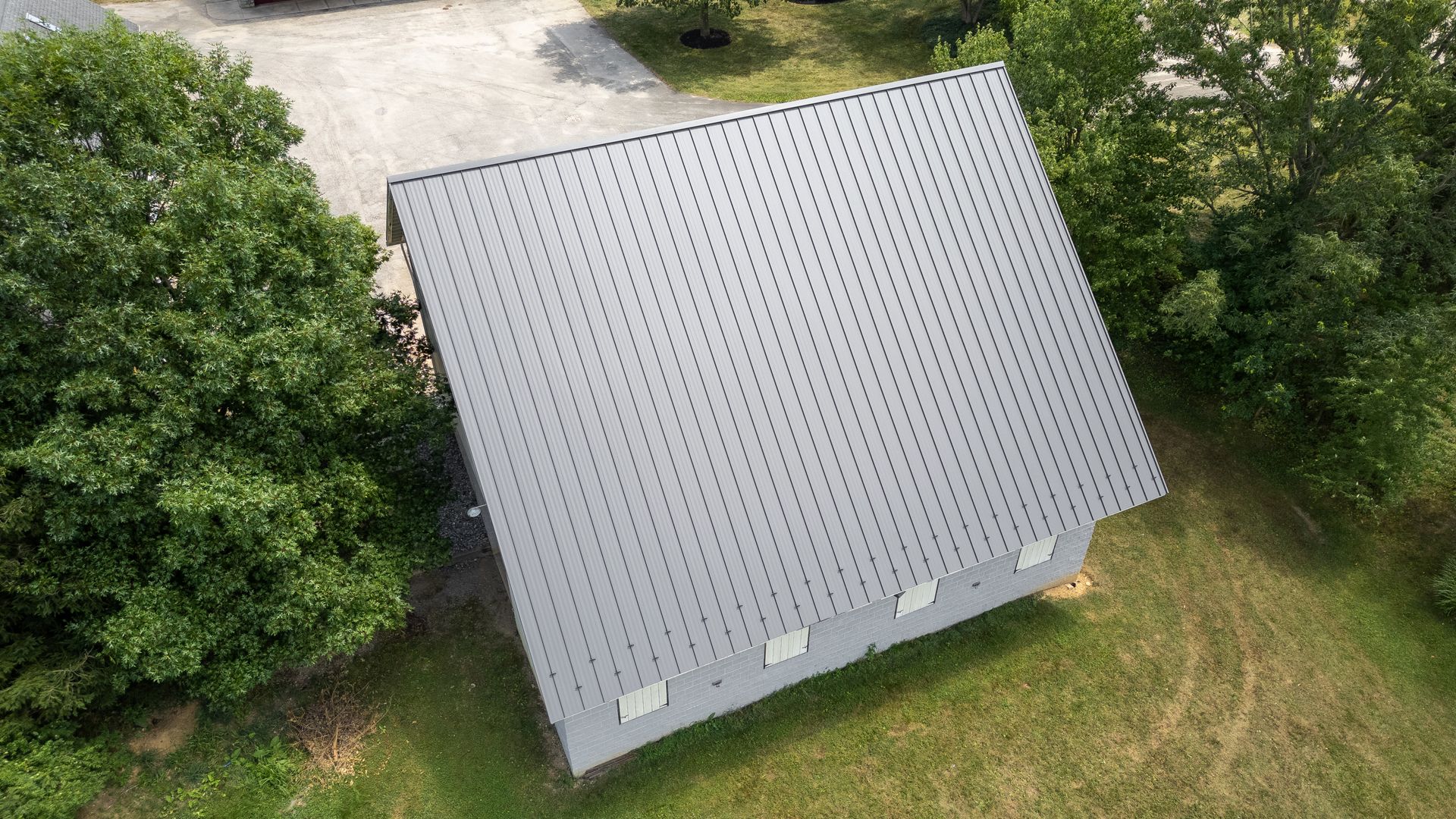 Gray metal roof on a white building, surrounded by green trees and grass.