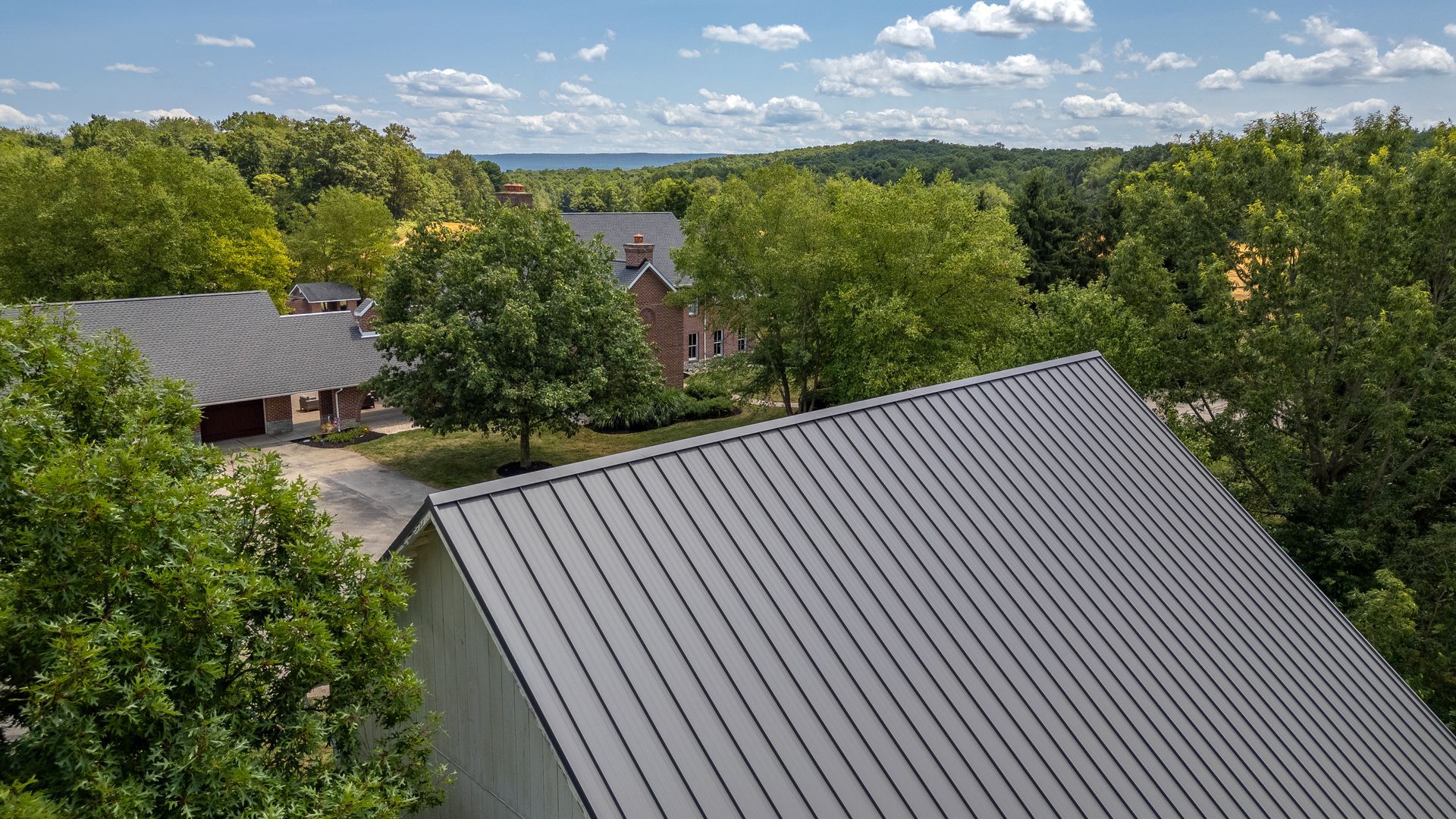 View of metal roof, trees, and distant houses on a sunny day.
