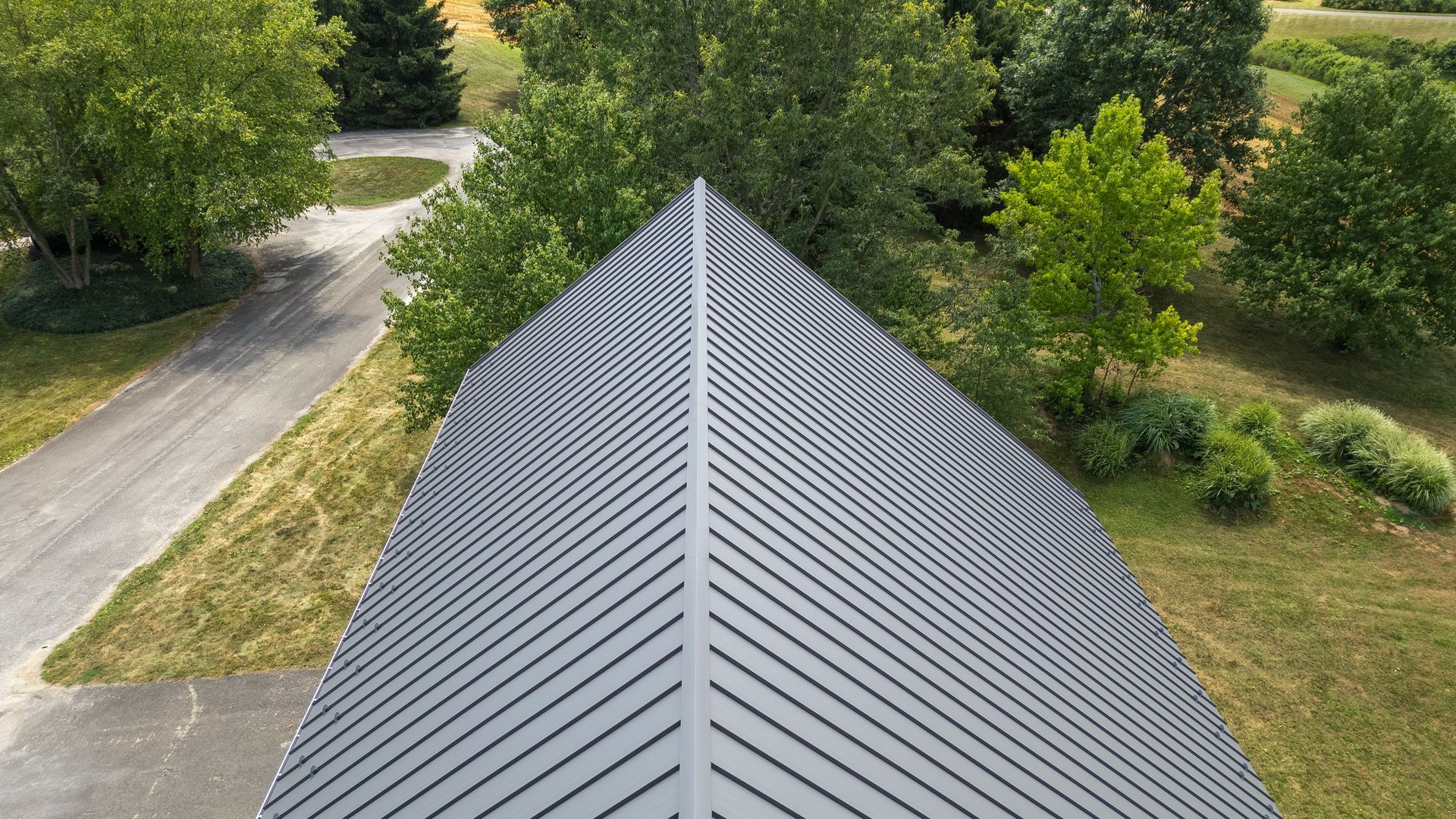 Gray metal roof with diagonal lines, surrounded by trees and a driveway.