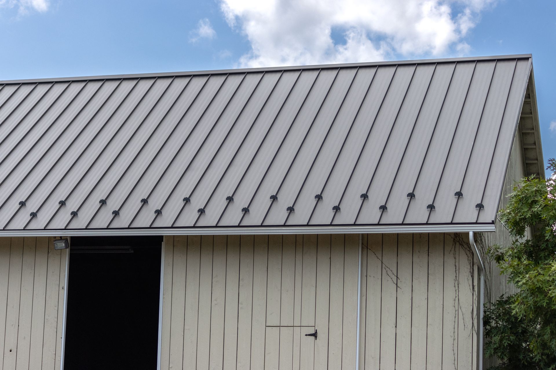 Gray metal roof on a light-colored building against a blue sky with some clouds.