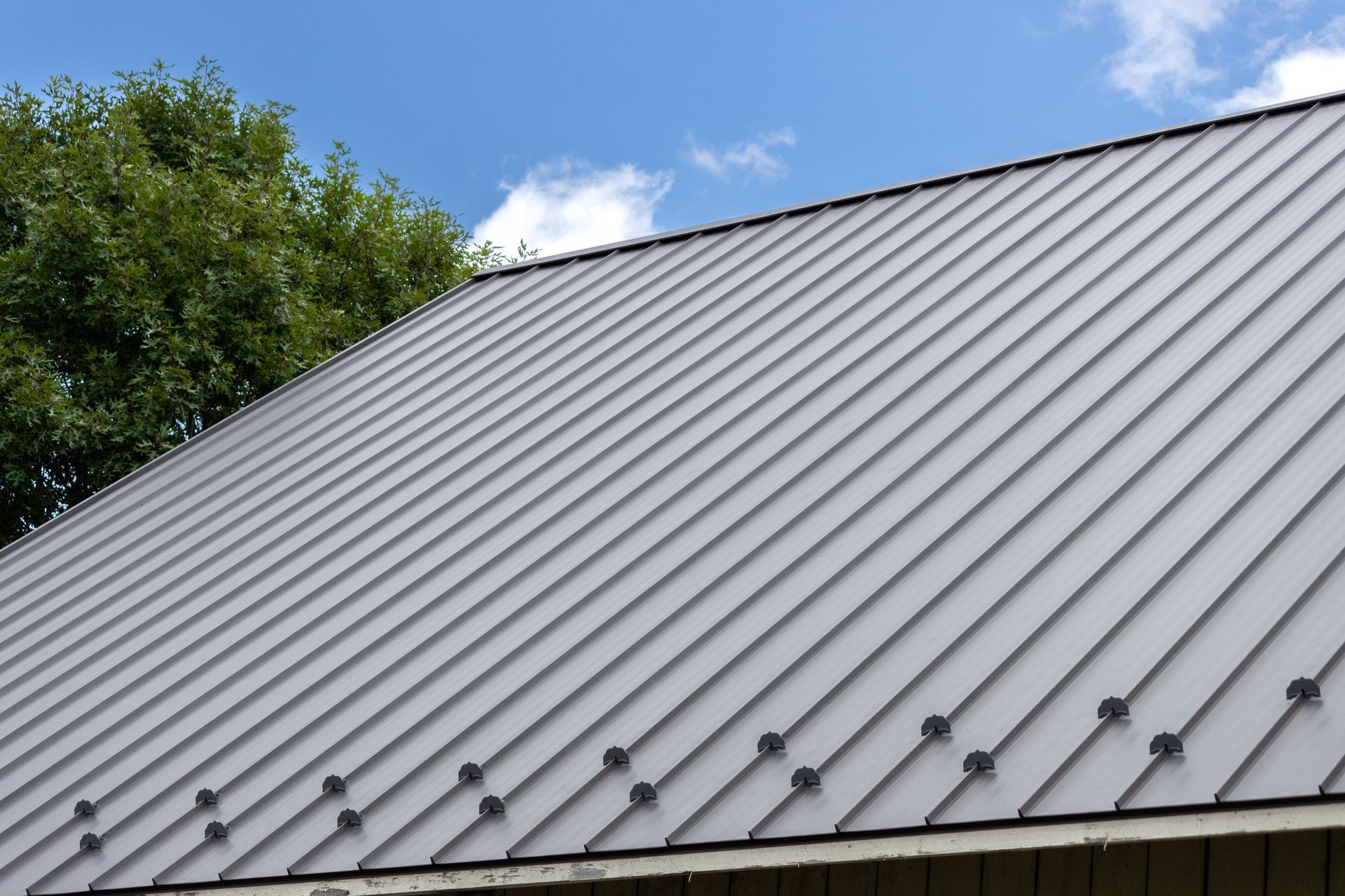 Gray metal roof with a cloudy sky and green tree in the background.