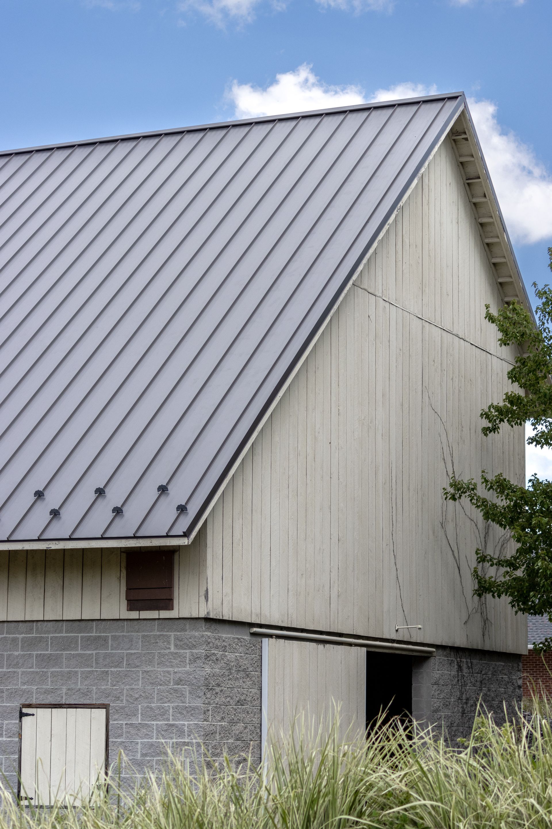 A light-colored barn with a gray metal roof, set against a blue sky.