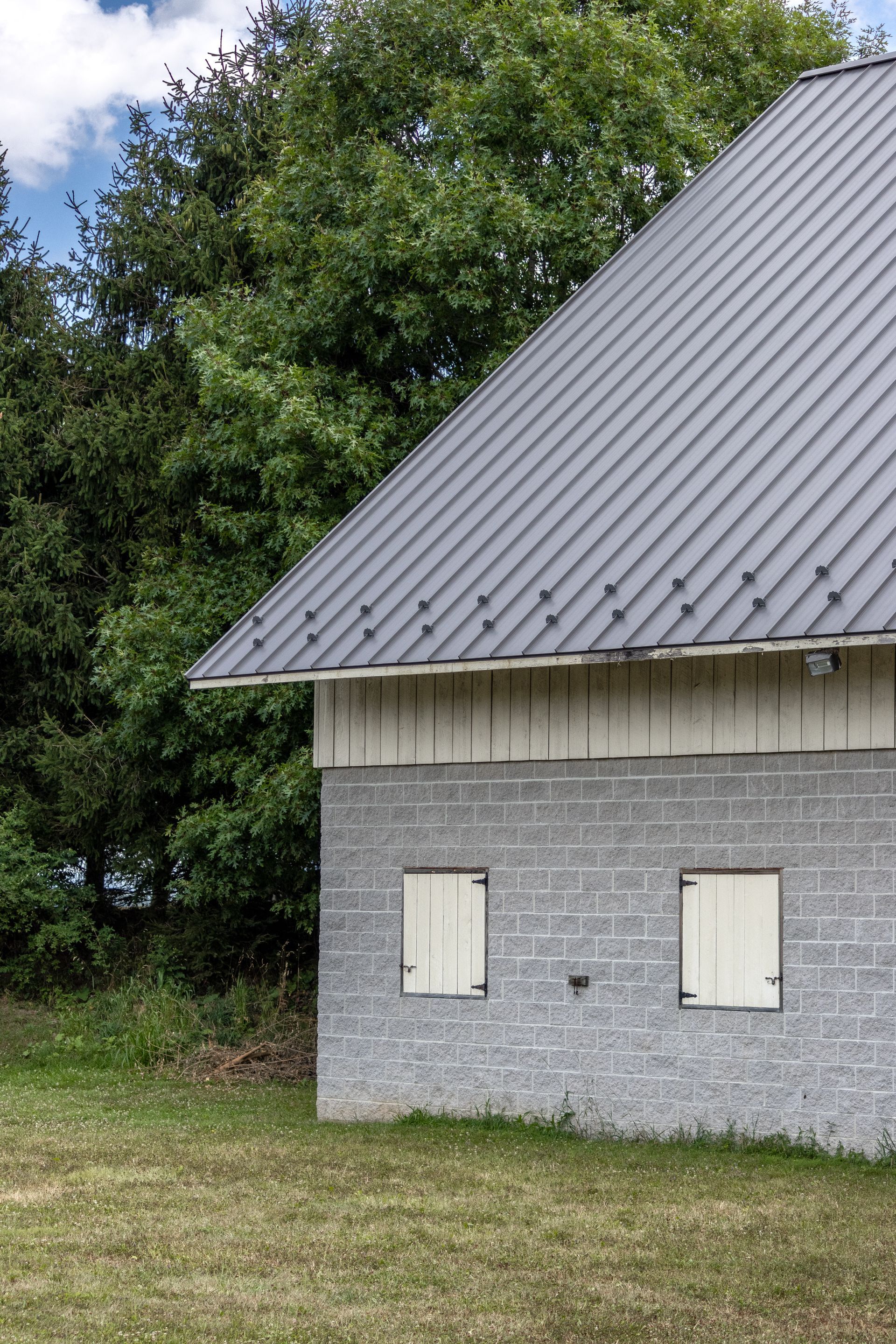 Gray block building with two shuttered windows, gray angled roof, and trees.
