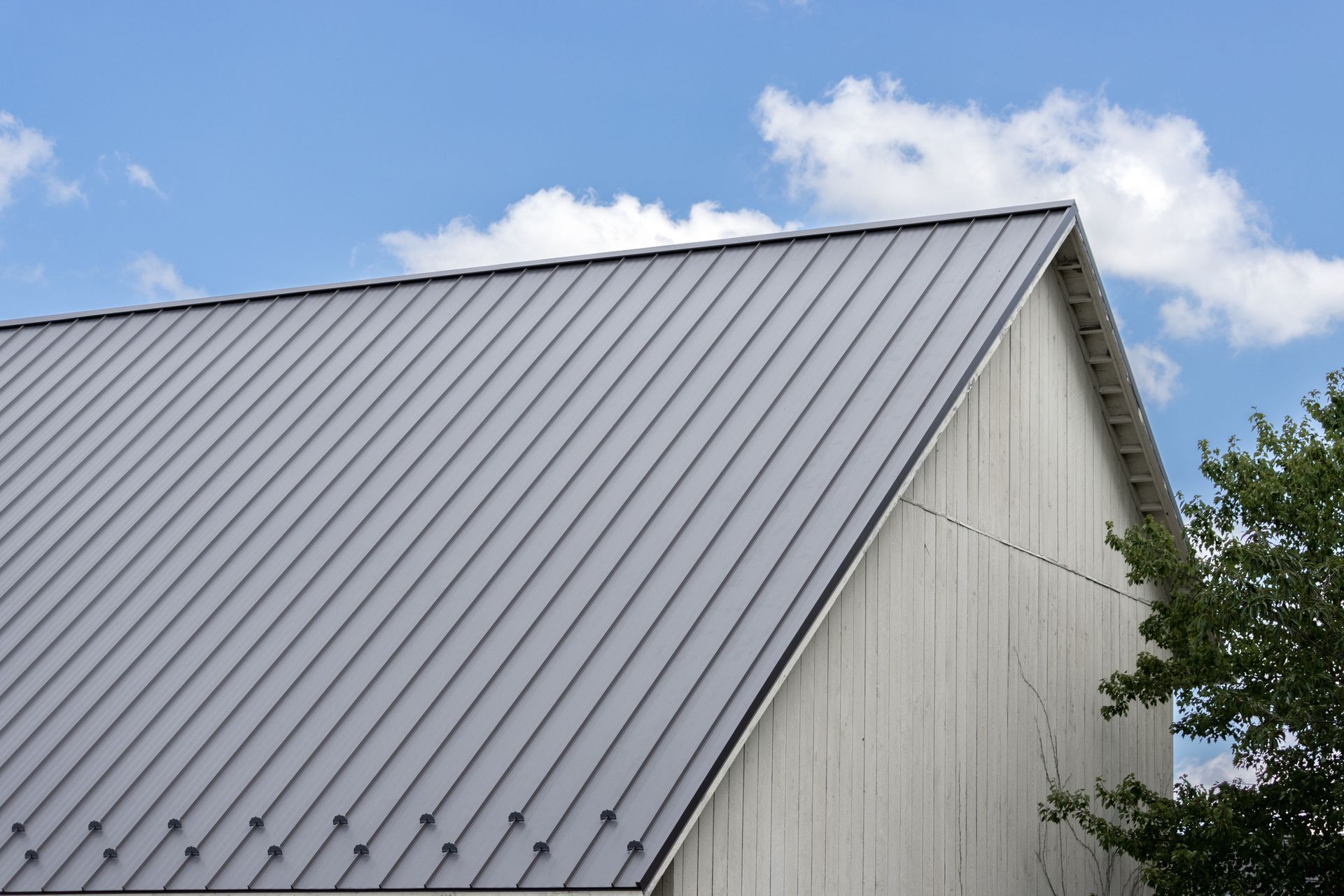 Gray metal roof on a white-sided building with a blue sky in the background.