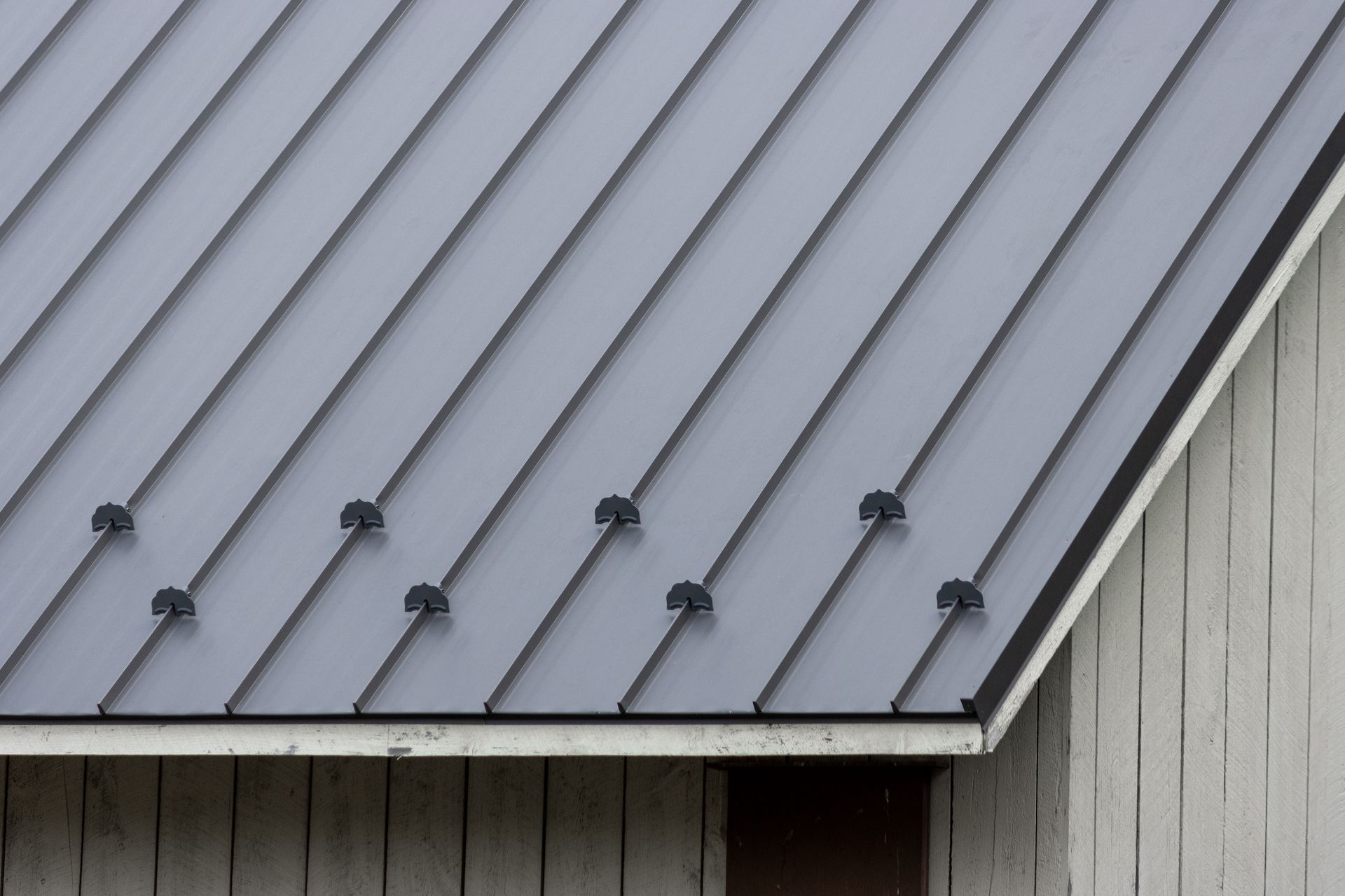Gray metal roof with black fasteners on a white wooden building.