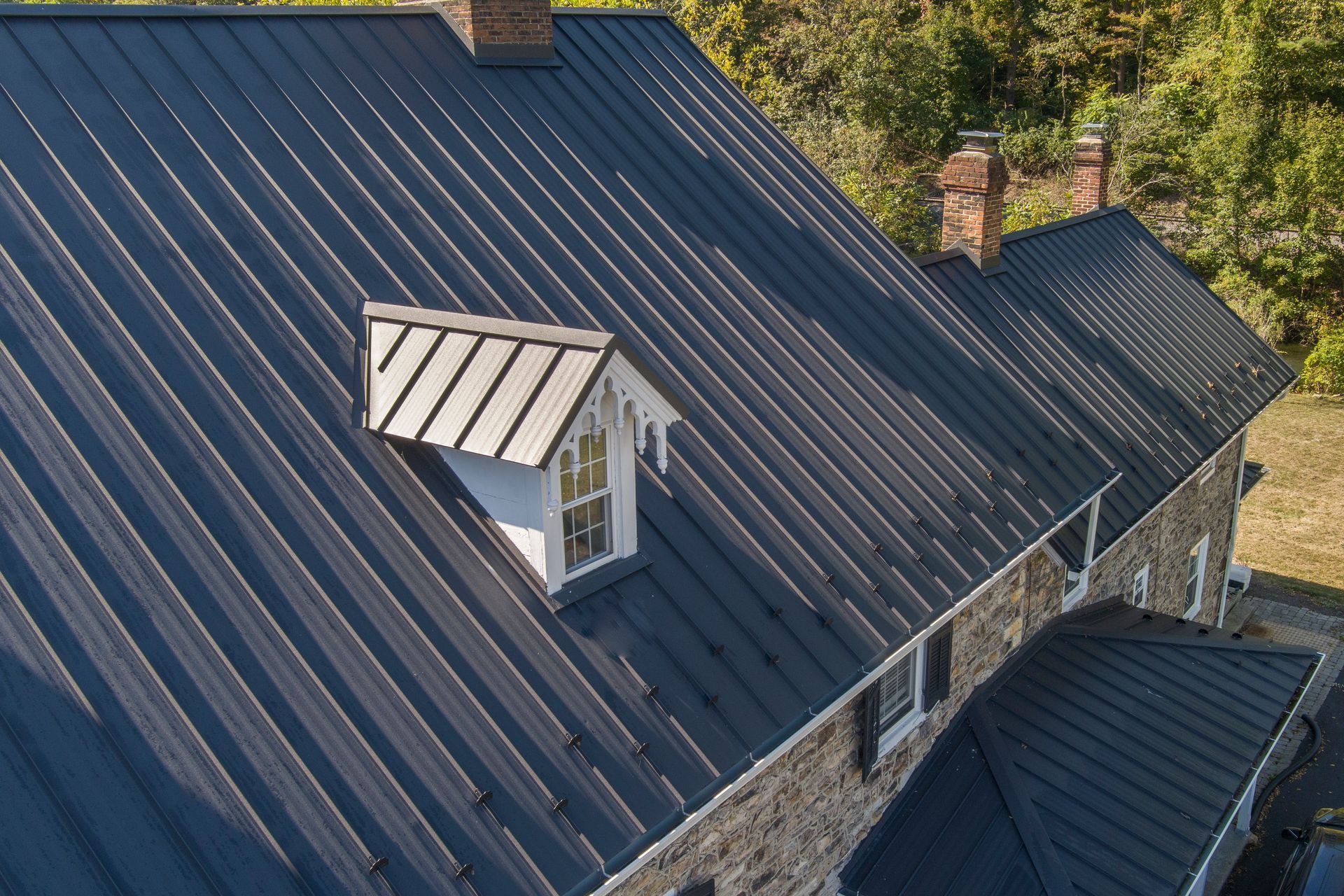 A stone house with a dark, vertical seam metal roof and a small dormer window.