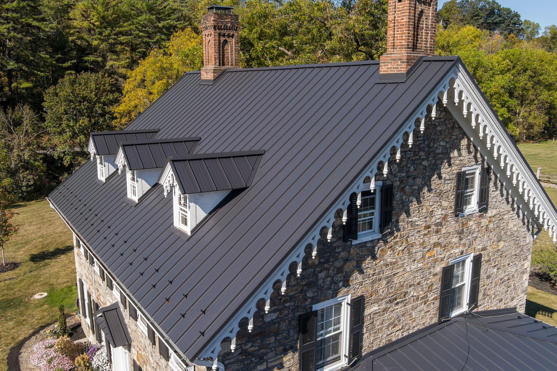 A historic stone farmhouse featuring a new dark standing-seam metal roof, decorative white trim, and multiple dormers.