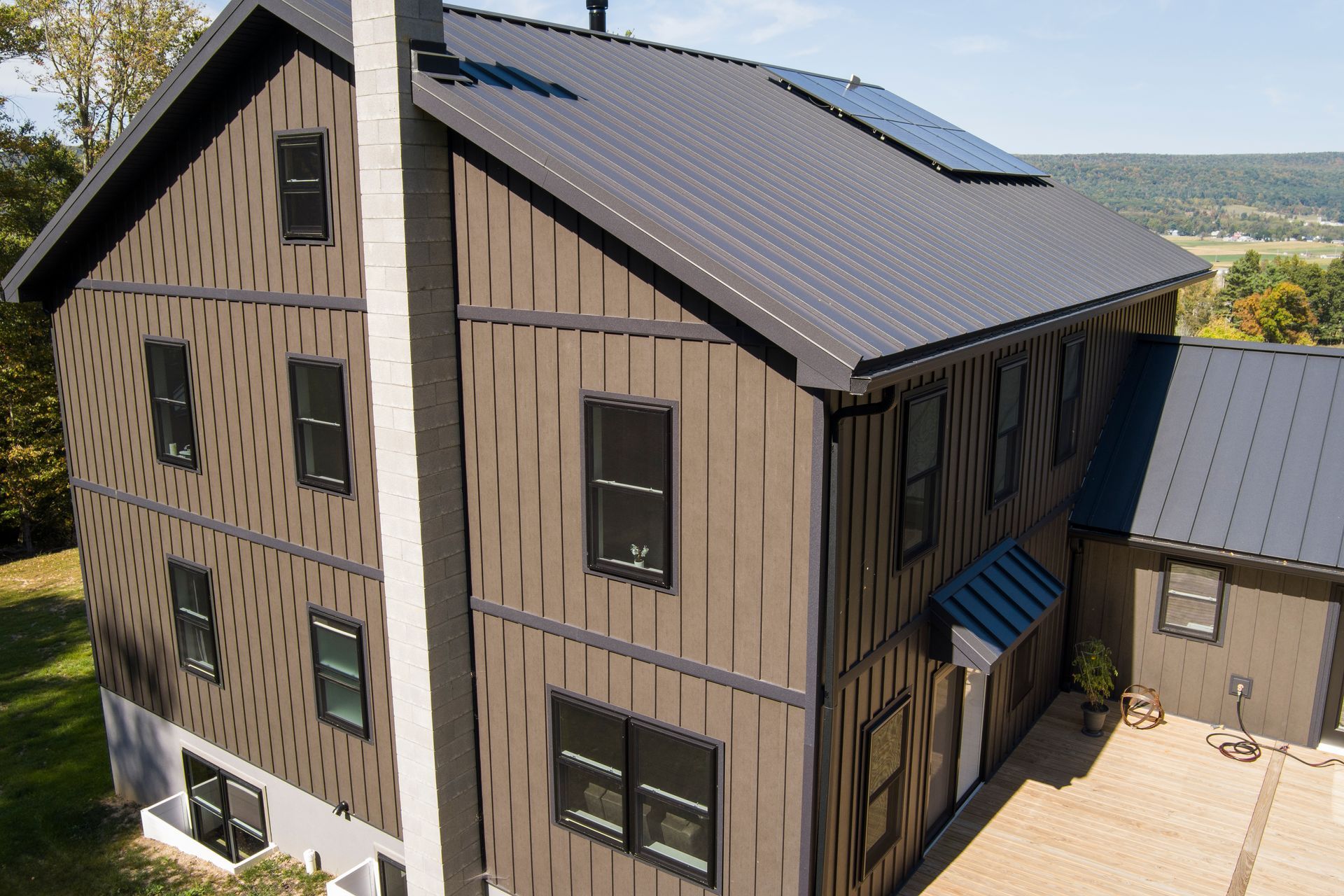 An aerial view of a three-story house with unique, dark vertical patterned siding and a dark metal roof.