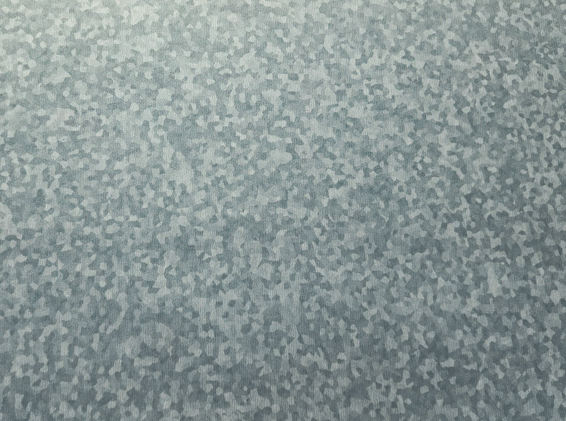 Close-up of galvanized steel sheet with mottled, speckled surface. Gray and silvery tones dominate.