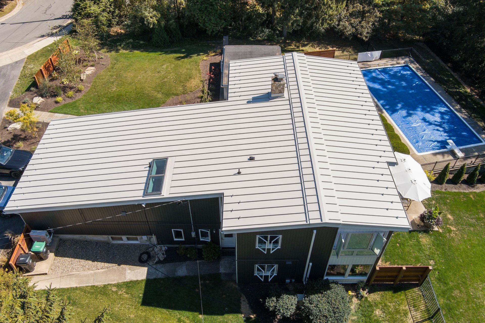 An aerial view of a dark-sided house with a light-colored metal roof featuring a distinctive, repeating curved pattern.