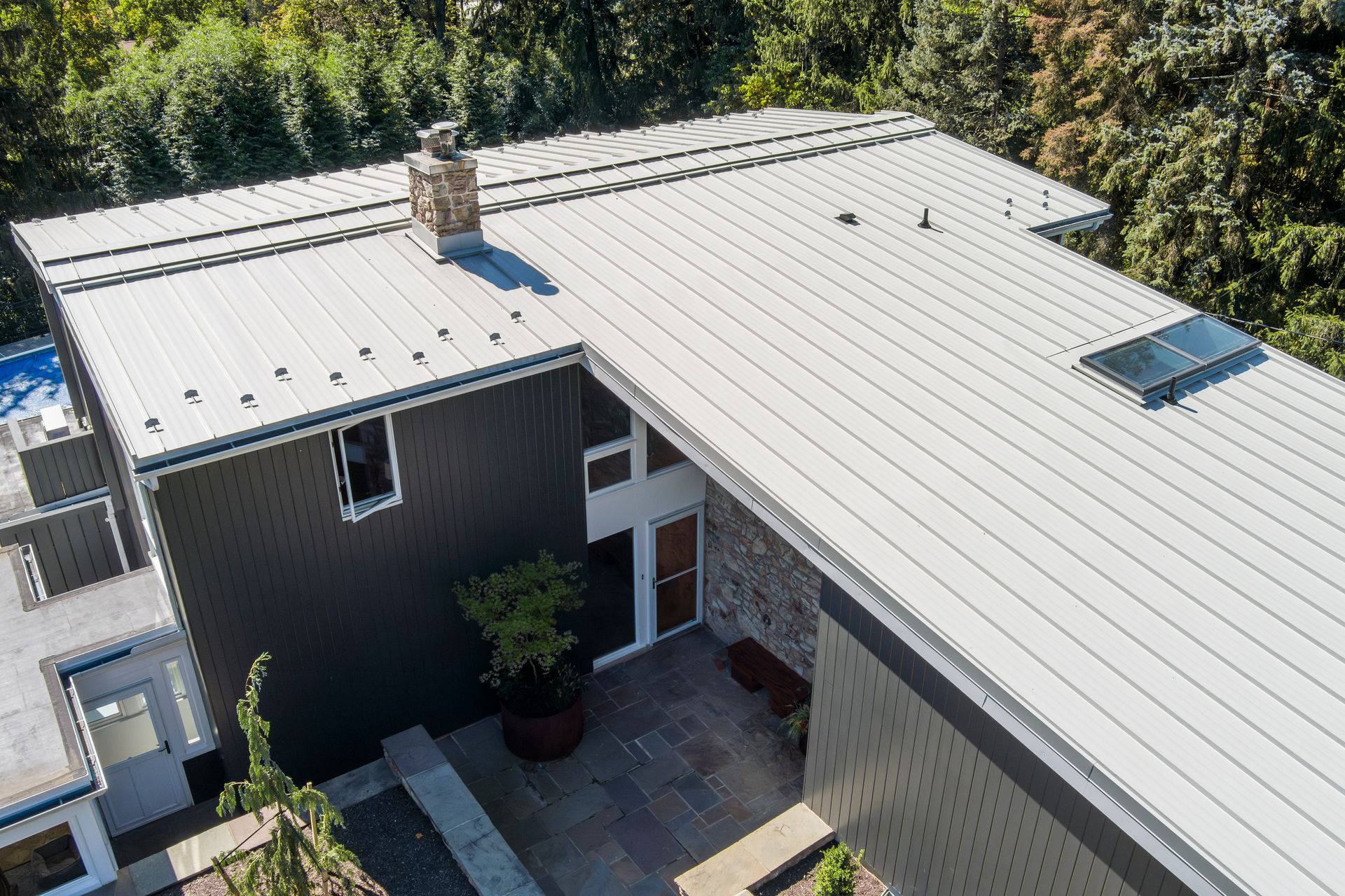 High-angle view of a modern house with a grey standing-seam metal roof, stone accents, and an entry courtyard.