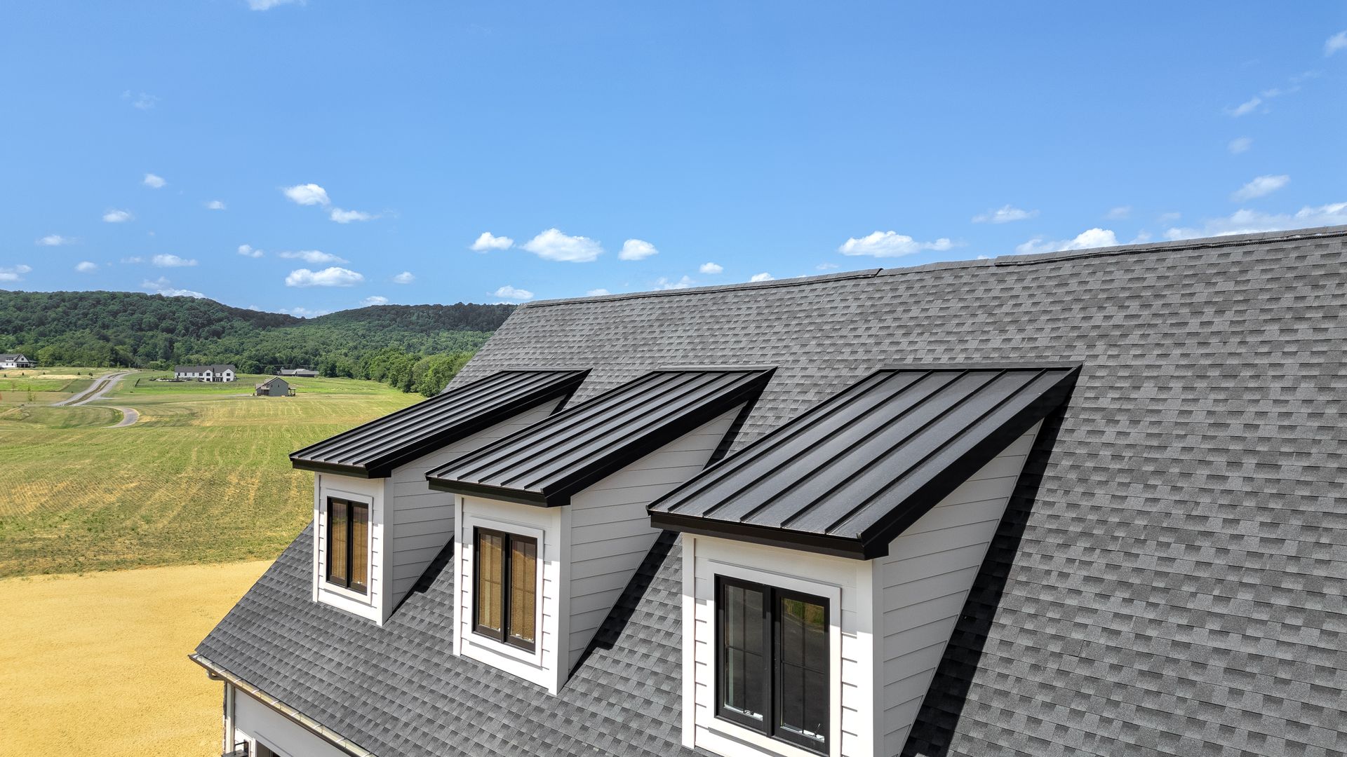 Three white dormer windows with black trim on a gray shingled roof against a blue sky.