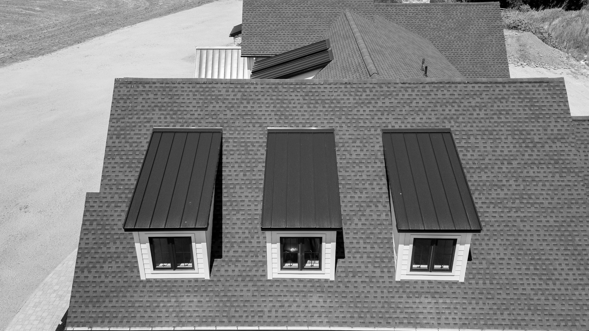 Three dormer windows with dark metal roofs on a shingled house roof.