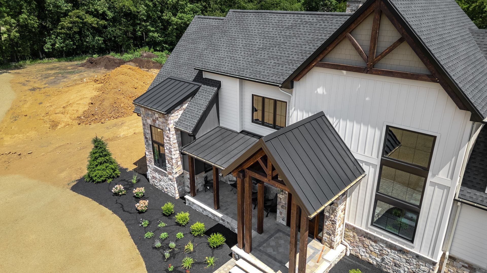 Modern house with stone accents, dark roof, and porch with wooden beams, in front yard.
