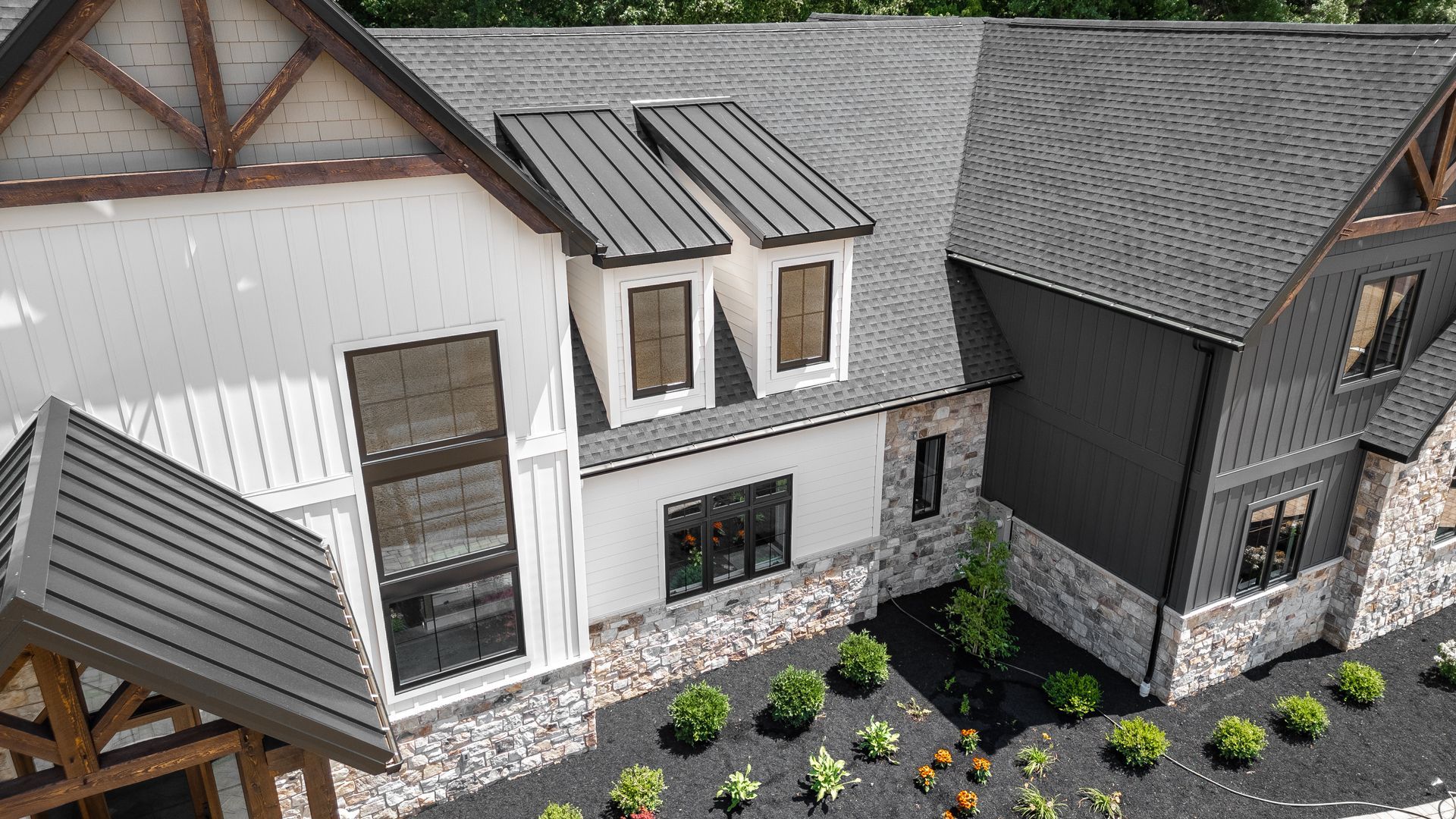 Modern house with gray metal roof and white/stone siding, black accents, and landscaping.