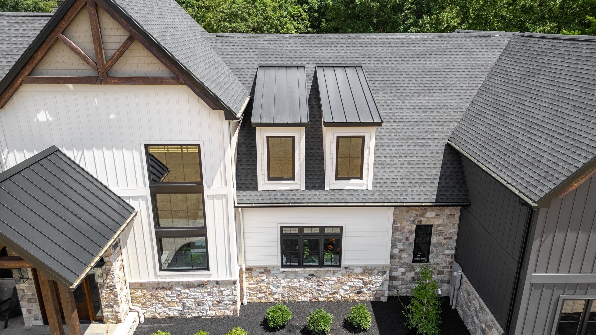 Modern home exterior with gray roof, white siding, stone accents, and black-framed windows.
