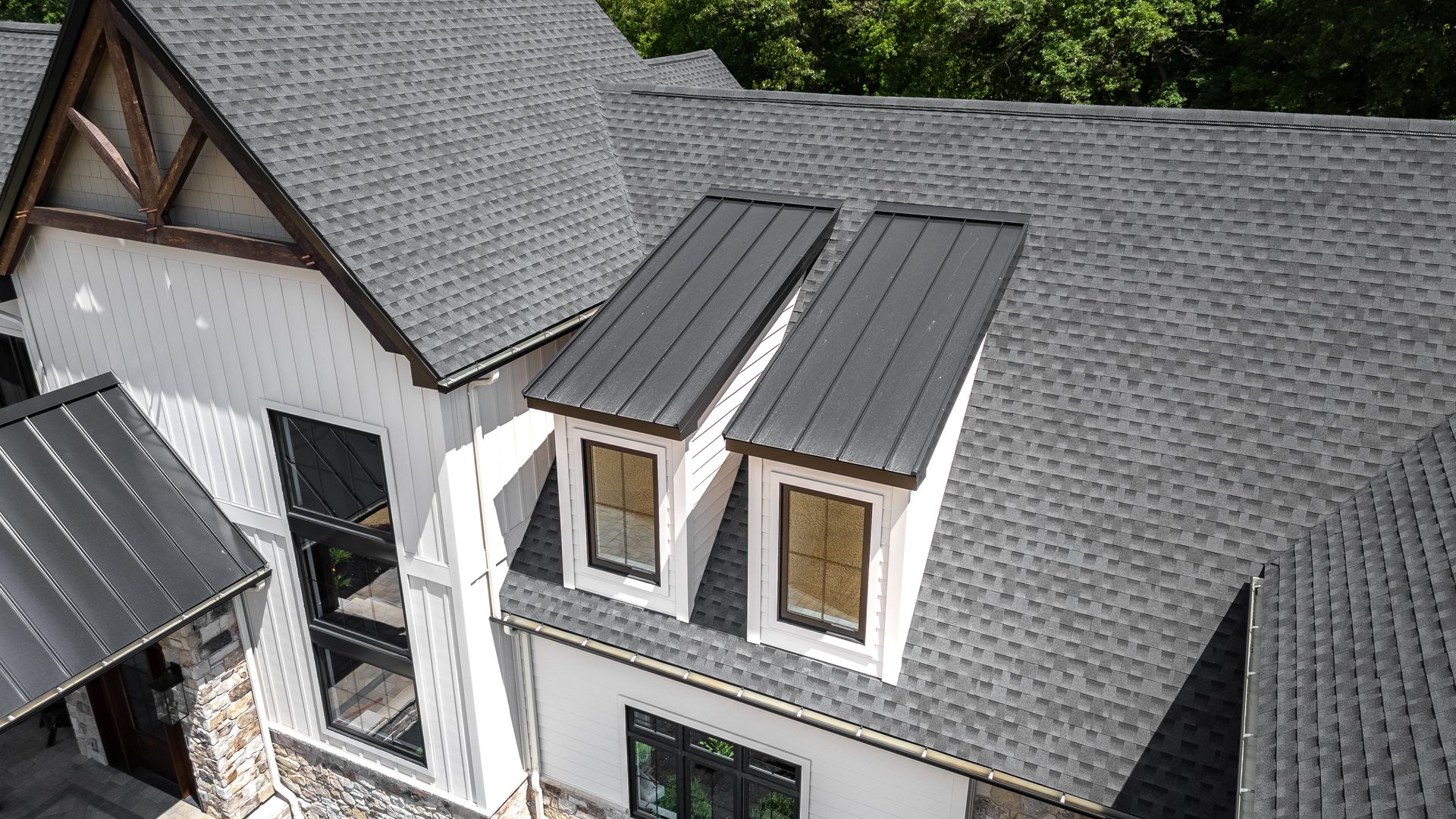View of a white house with grey shingle roof and black dormers, sunny day.