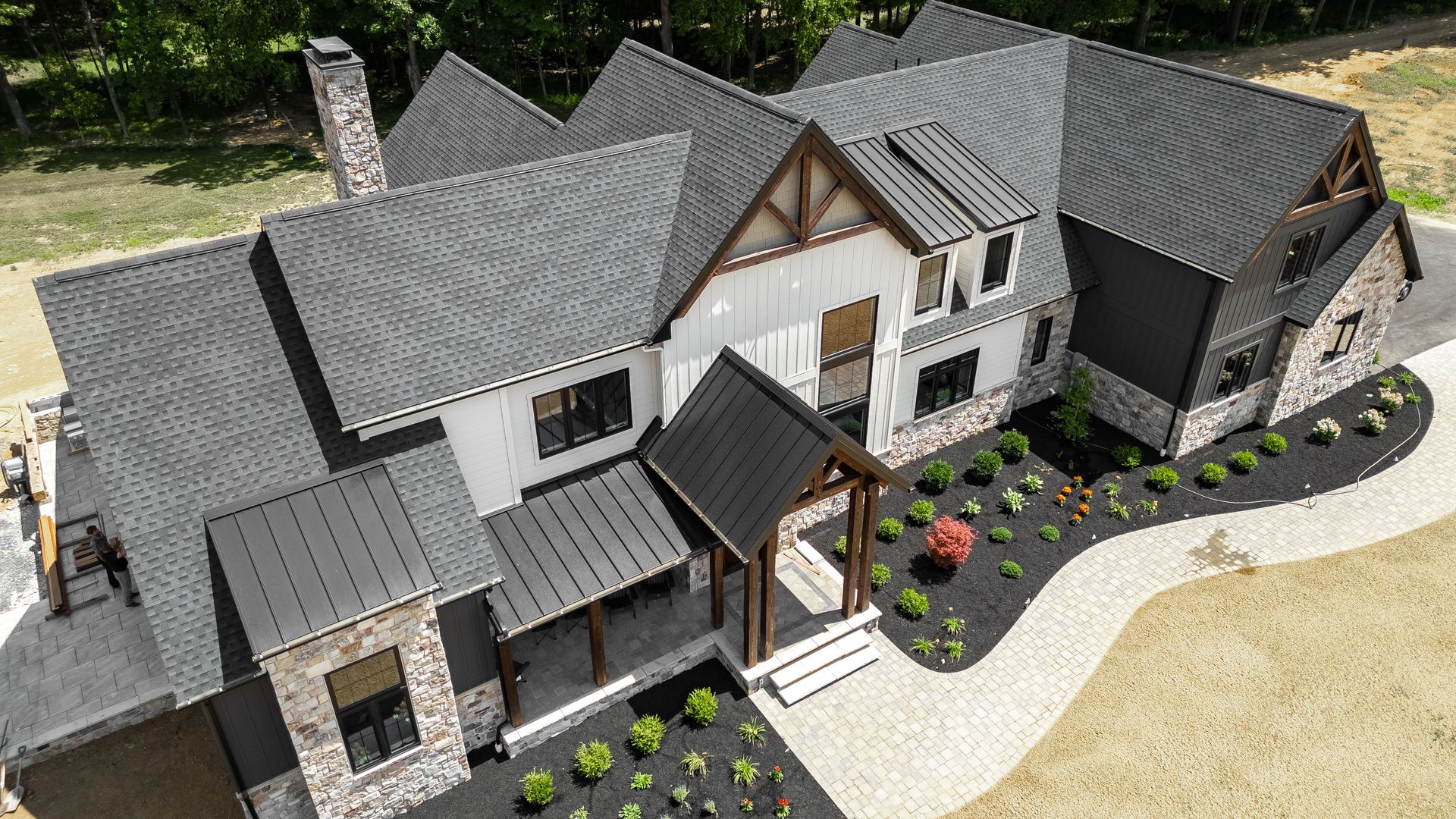 Modern two-story house with gray roof, stone accents, and black trim, surrounded by landscaping.