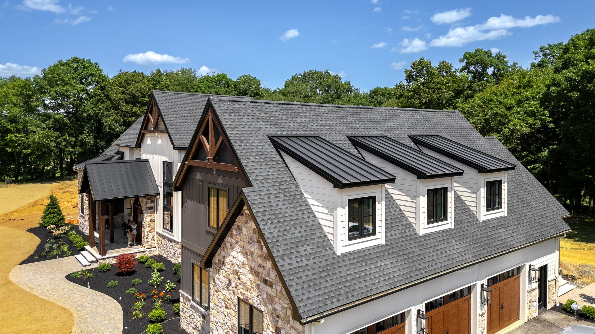 House with dark roof, stone and wood siding, surrounded by trees on a sunny day.