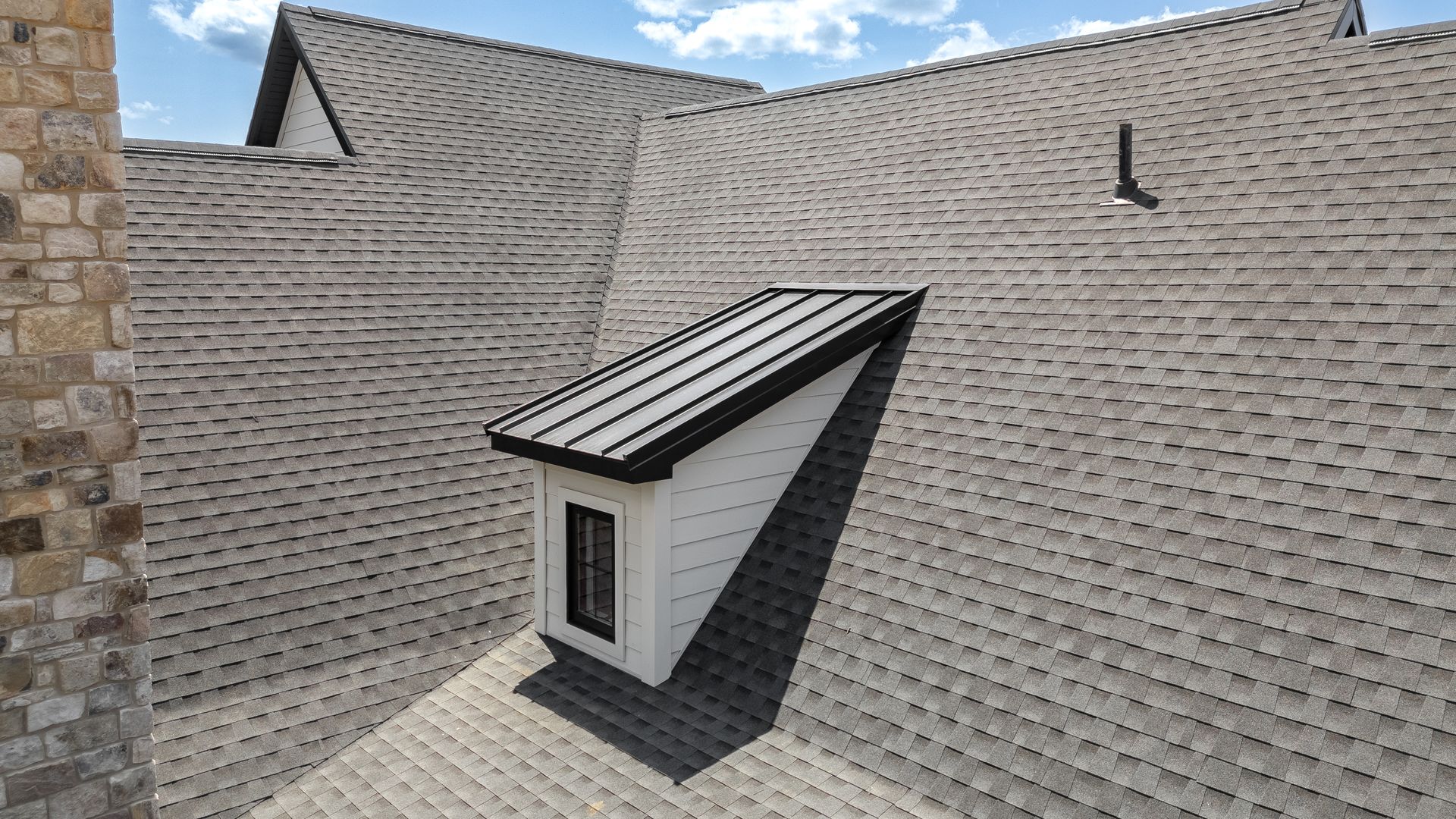 A view of a roof with shingles and a small window. The window has a black frame.