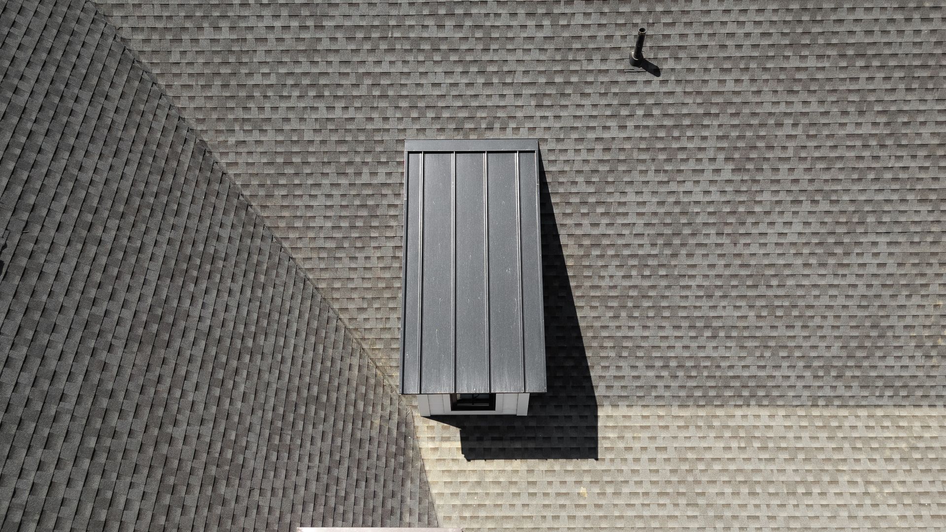 Bird flies over a gray roof with a metal vent.