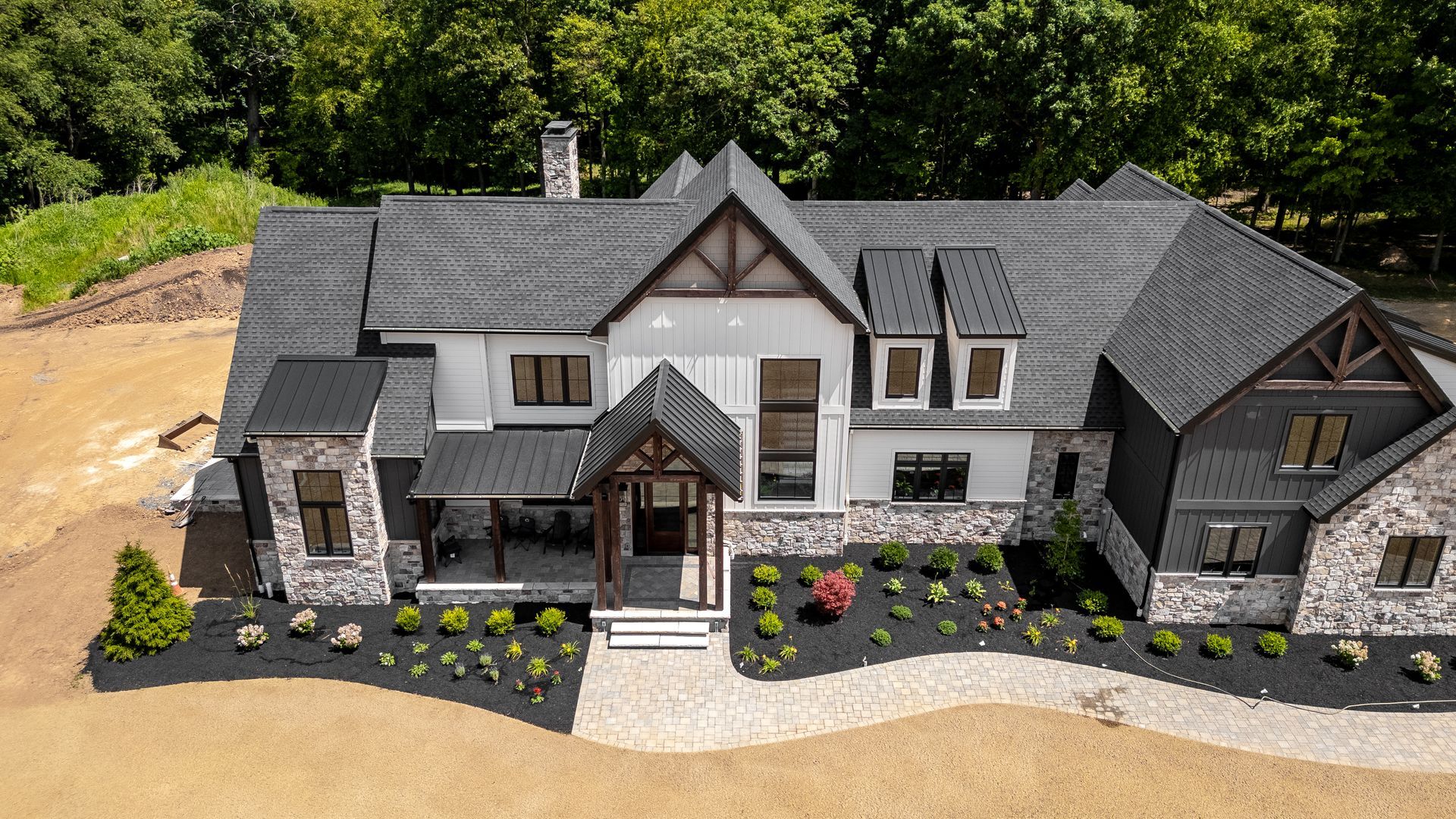 Luxurious two-story home with gray roof, stone accents, and manicured landscaping.