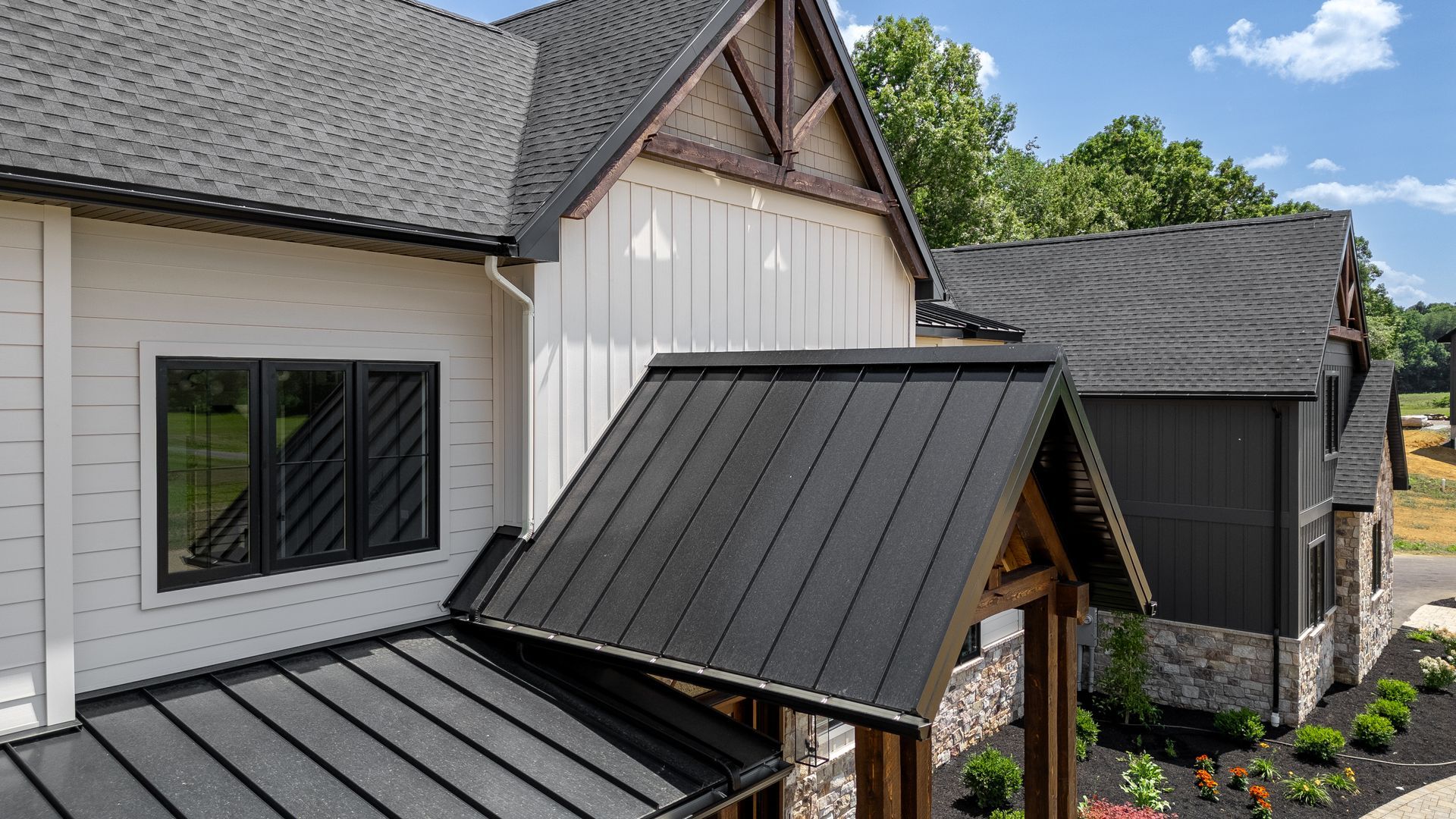 Black metal roof of a modern house with white siding, black windows, and stone accents.