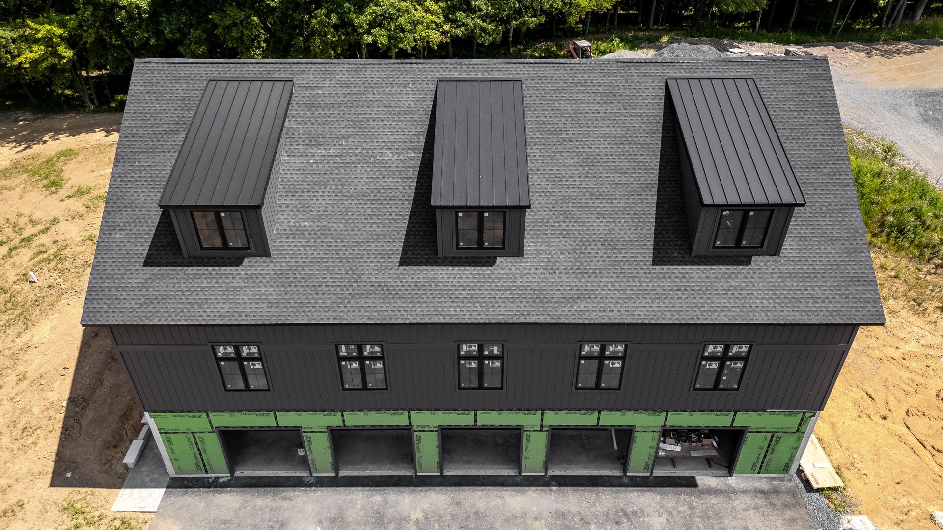 Black house with three dormers, six windows, and open garage doors. Green wrap around base.