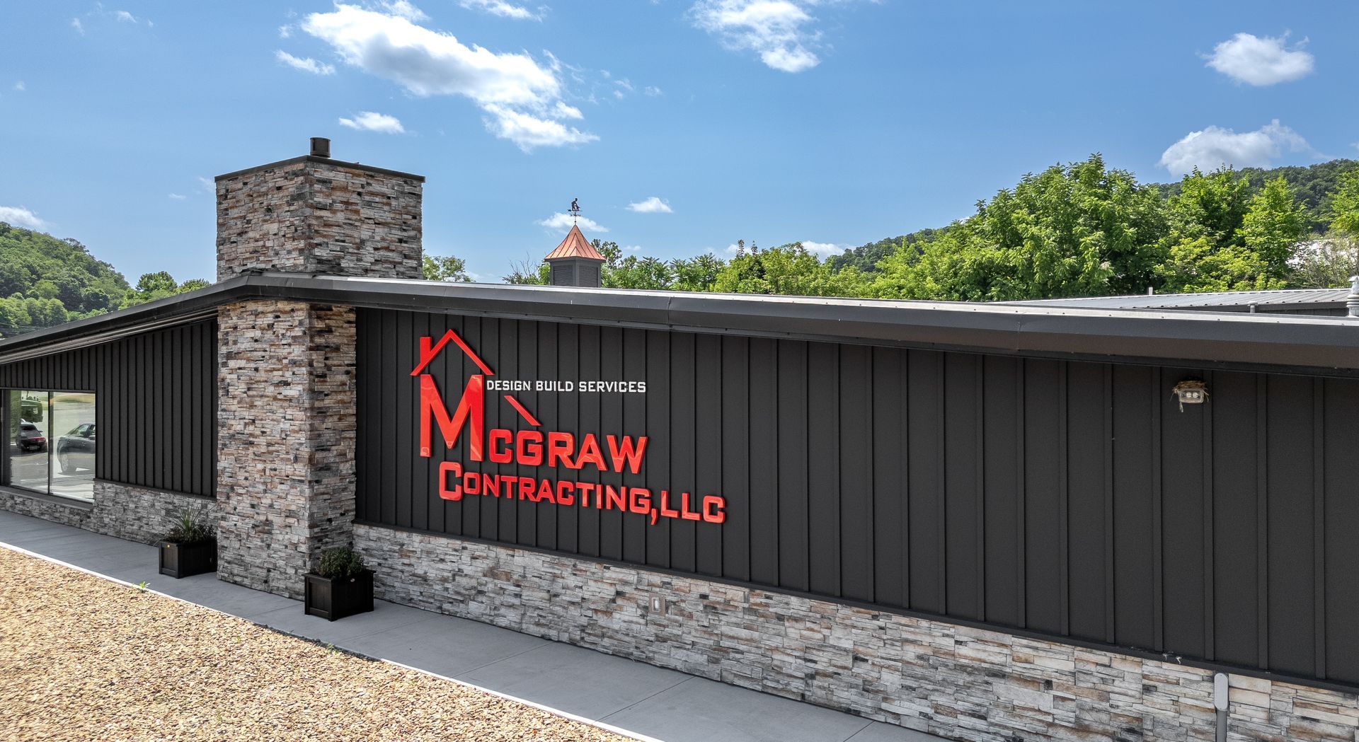 Exterior view of McGraw Contracting LLC building, with dark gray siding and red logo. Stone accents and a chimney.