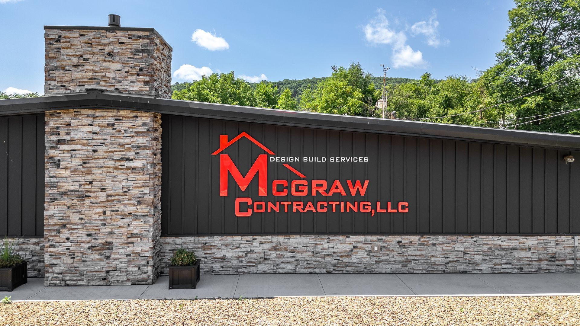 McGraw Contracting, LLC sign on a dark building with a stone chimney, under a blue sky.