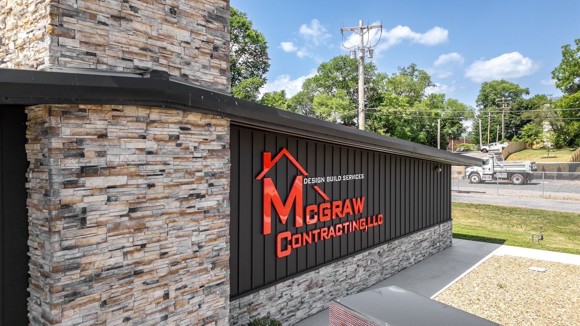 Sign for McGraw Contracting LLC with a red logo, set in a building with stone and black siding.