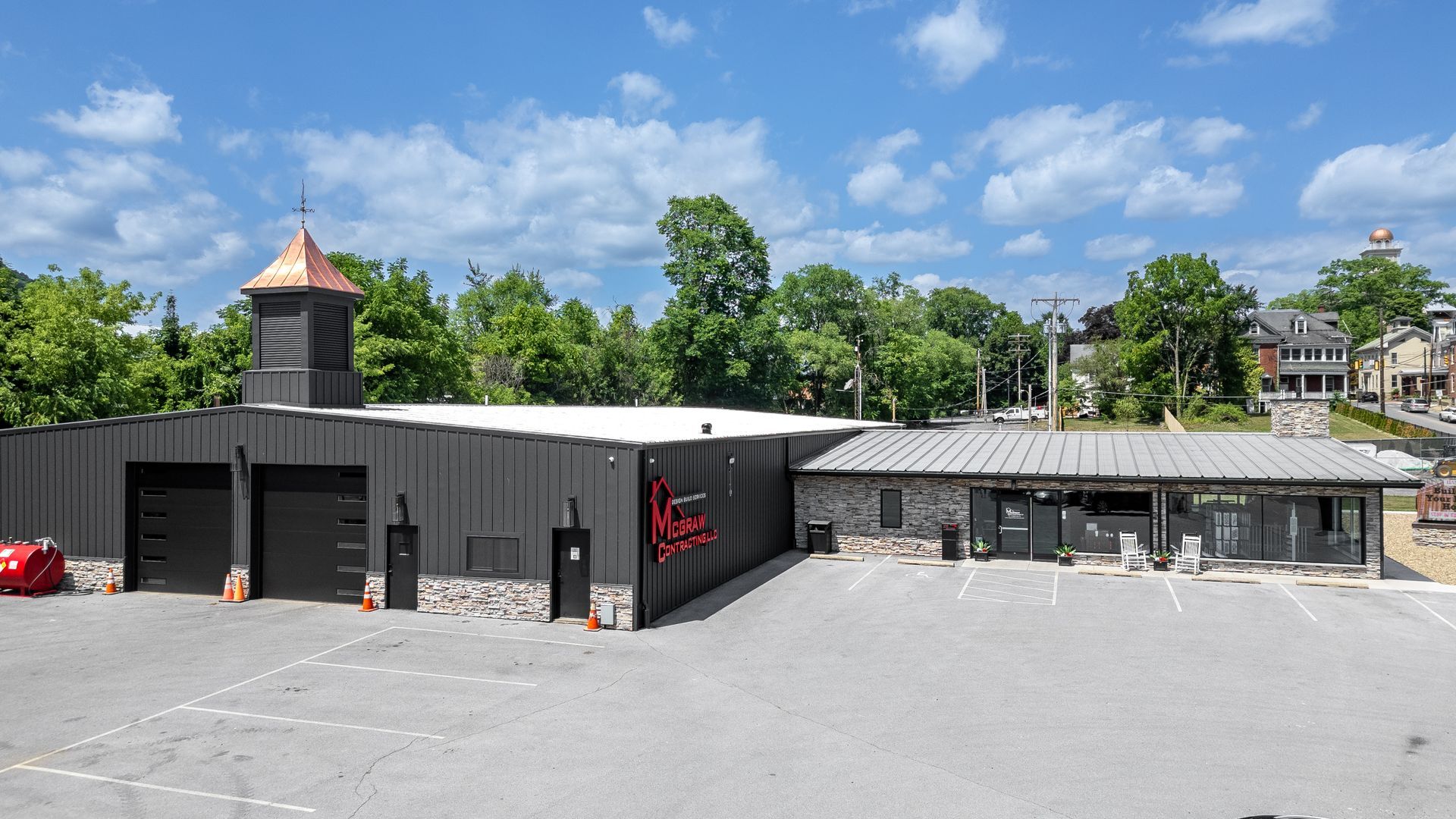 Modern gray commercial building with copper-topped tower, storefront, and large parking lot against a blue sky.