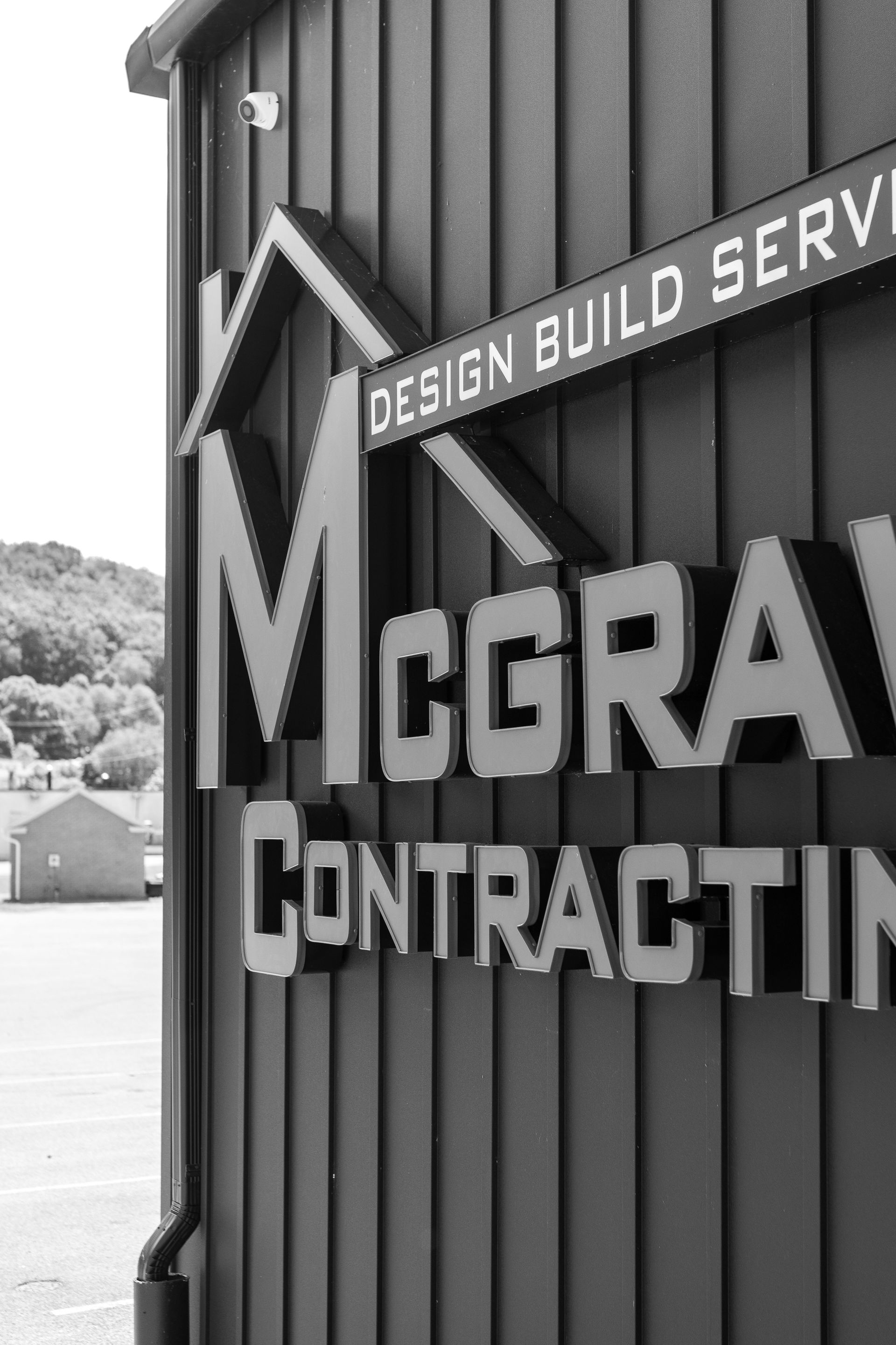 Close-up of McGraw Contracting sign with Design Build Services, building and trees in