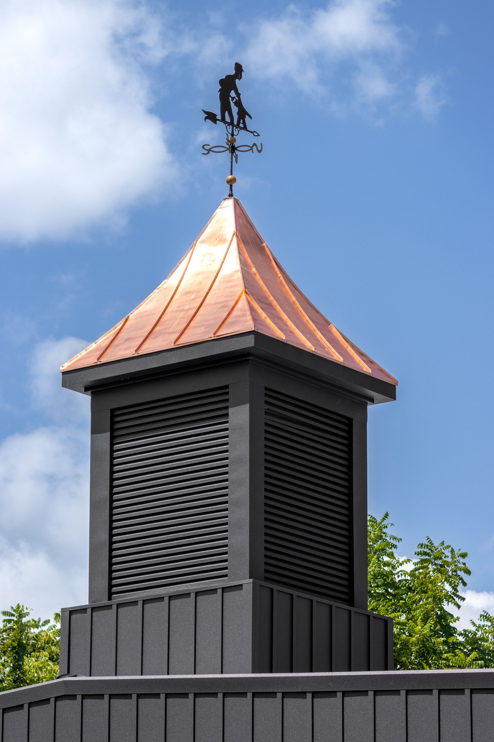 Copper-roofed black structure with weather vane on top; blue sky background.