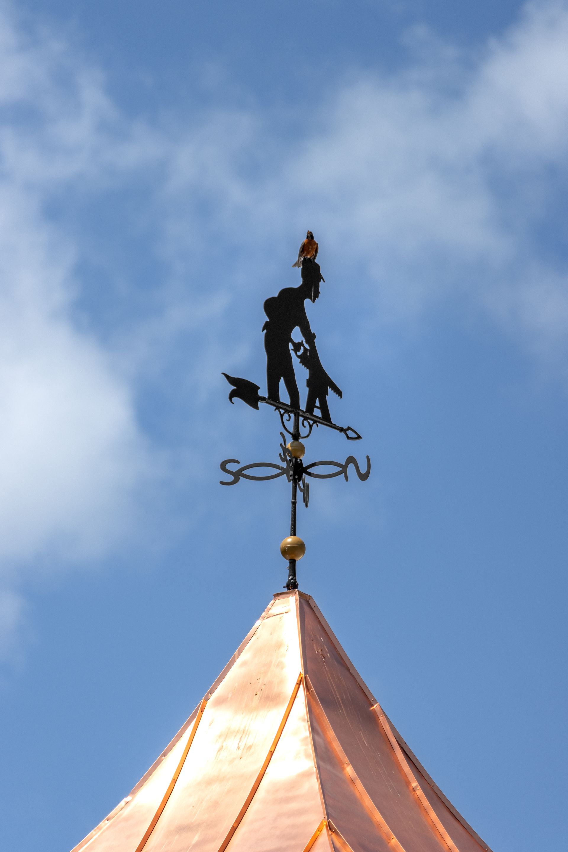 Weather vane with a silhouette of a person with two children, copper roof, blue sky.